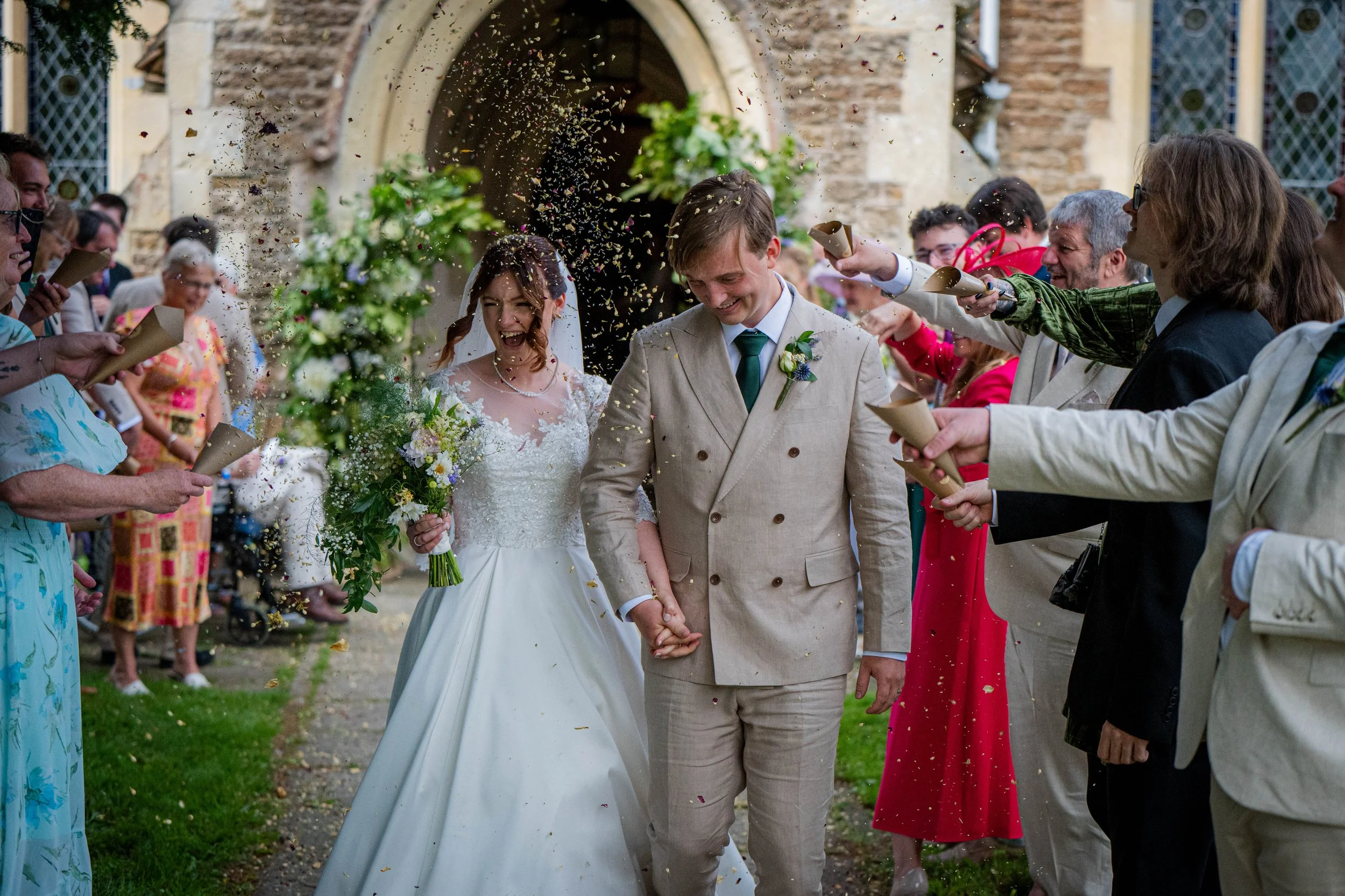 Bride and groom holding hands walking through guests throwing confetti outside of a church.