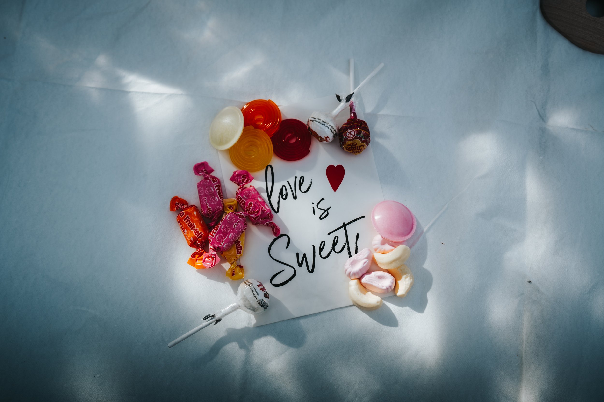Candy on a white paper with the word 'love' written on it, surrounded by pink, white, red, orange, and purple candies, with a pink heart-shaped candy at the bottom.