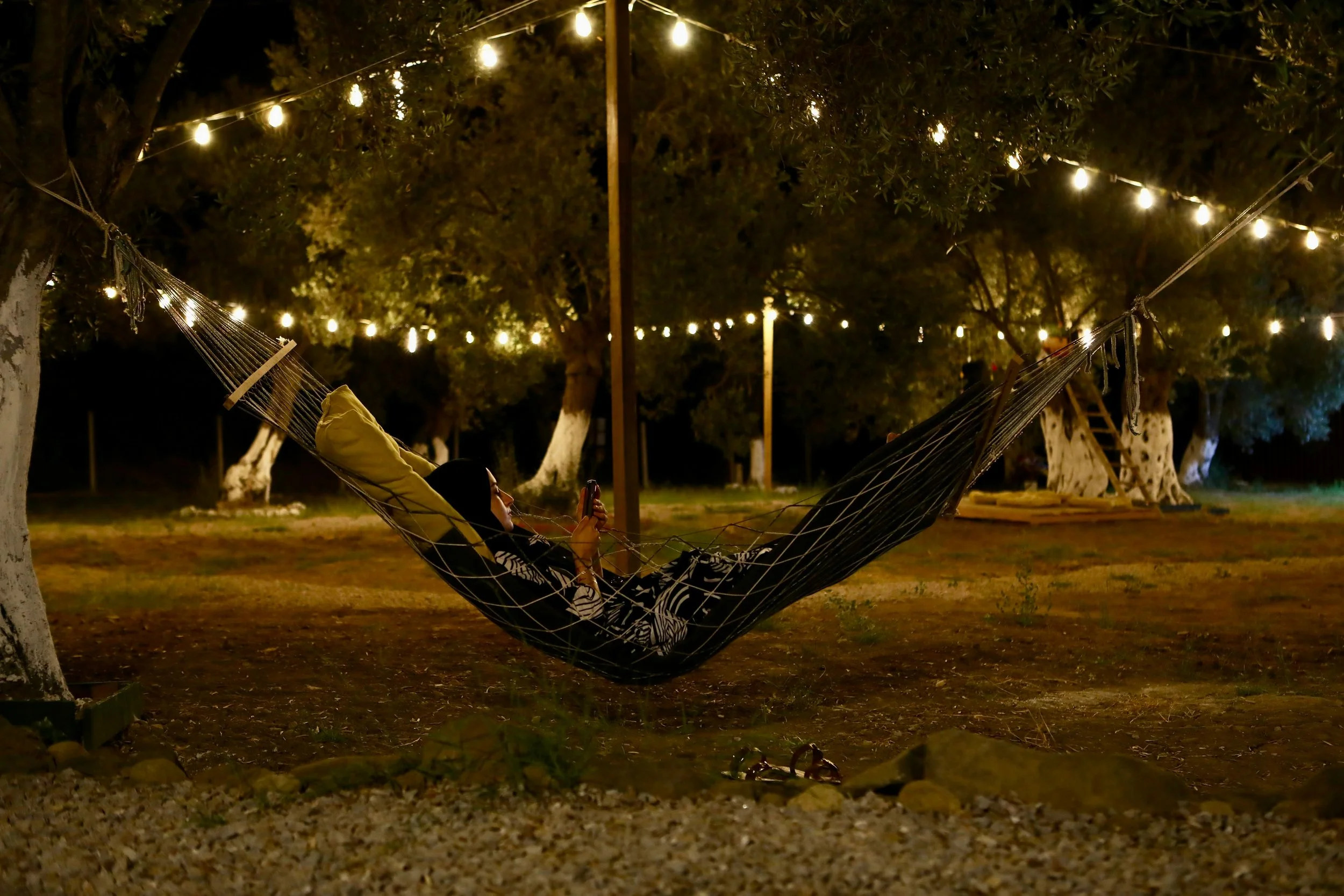 The 7 Types of Rest - a lady resting scrolling on her phone in a hammock at night