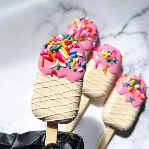 Four ice cream bars with pink icing and colorful sprinkles on a marble surface.