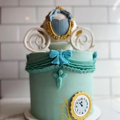 A cake decorated with a princess figurine wearing a blue dress and gold jewelry, with a mint green base and a clock design on the front.