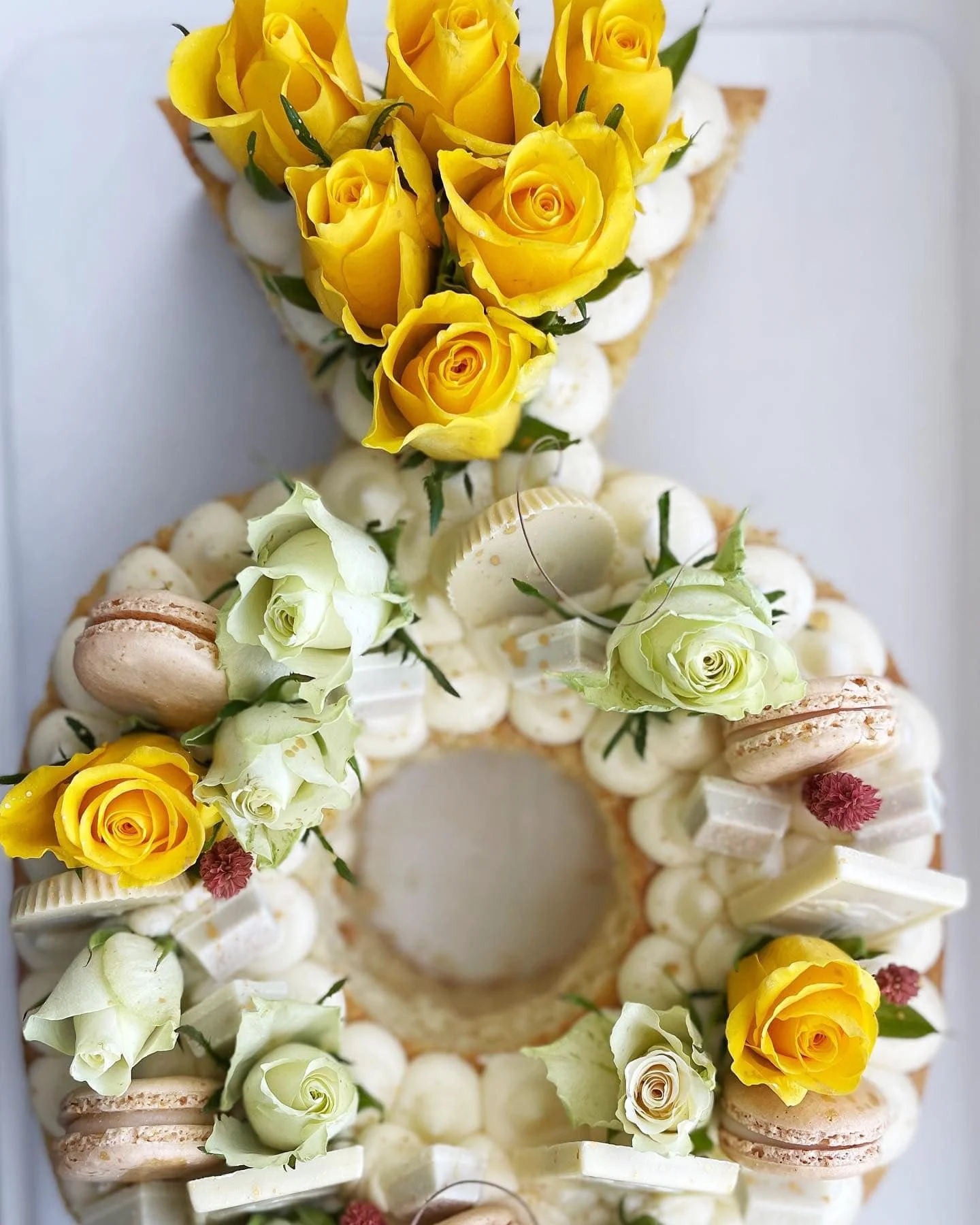 A floral cake decorated with yellow and white roses, macarons, and small flowers.