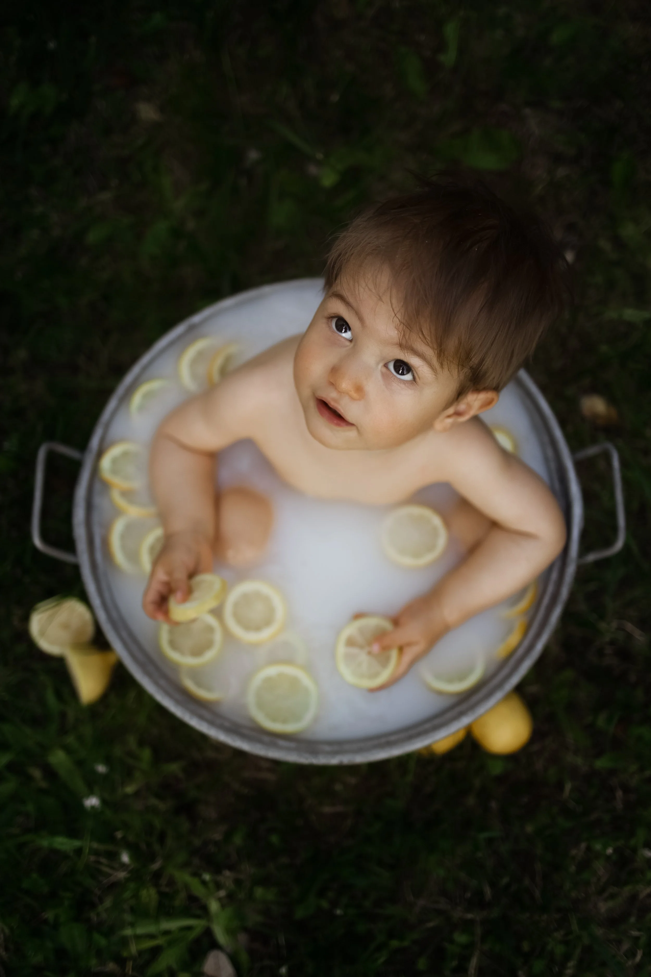 Un jeune garçon, vu de dessus, dans un bain de lait avec des rondelles de citron, à l'extérieur, sur l'herbe