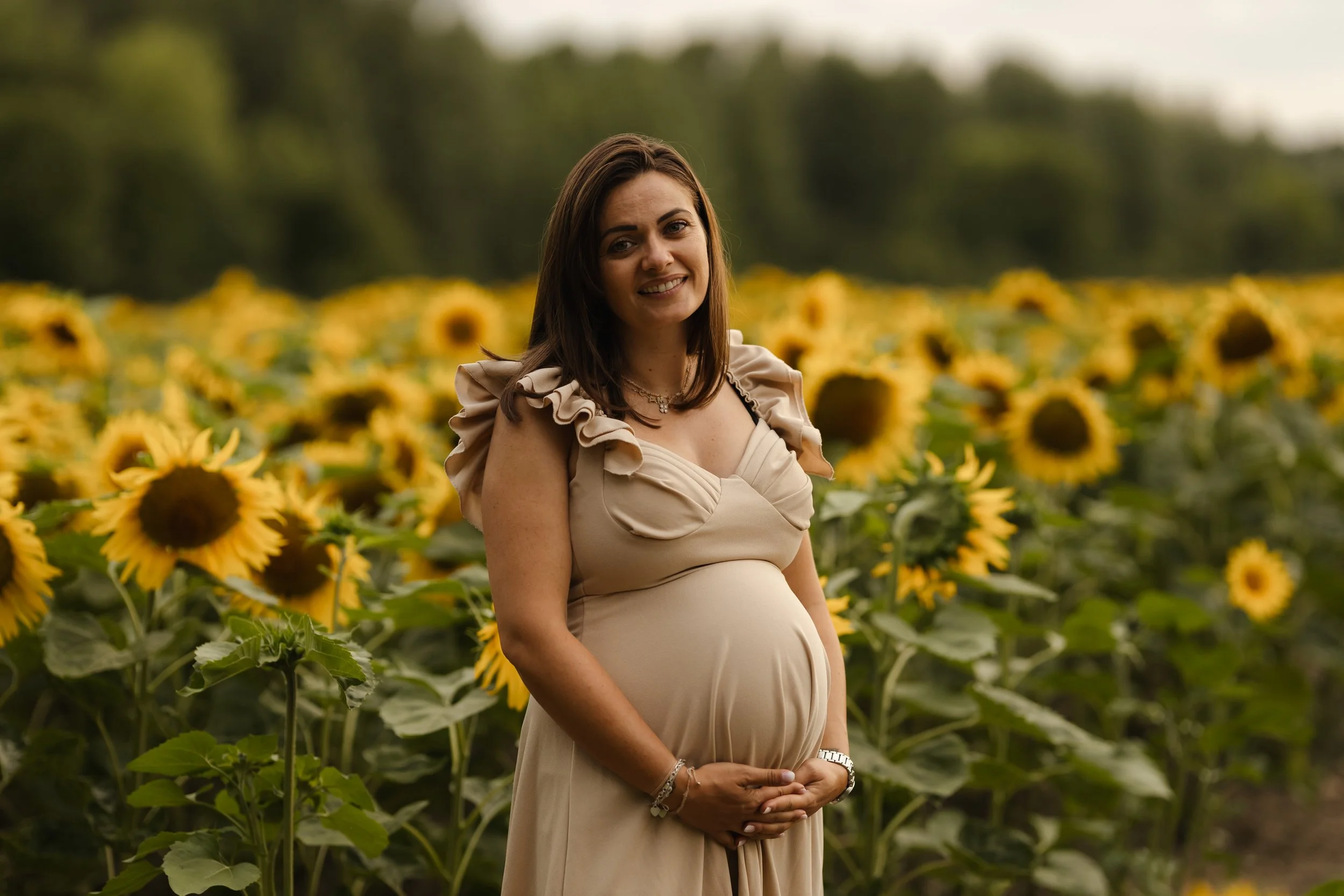 Femme enceinte souriante posant dans un champ de tournesols