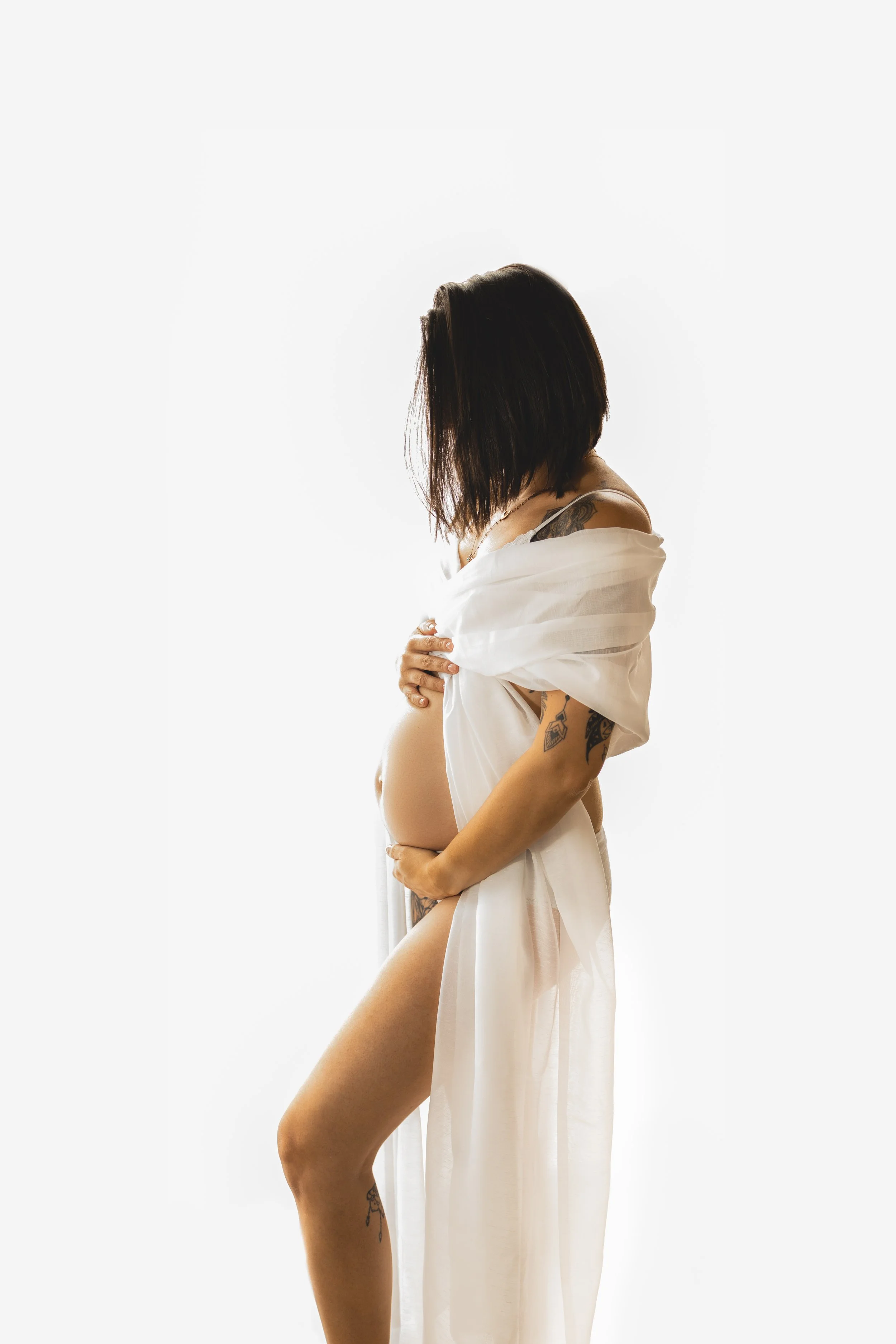 Femme enceinte portant une robe blanche semi-transparente, vue de profil contre un fond blanc