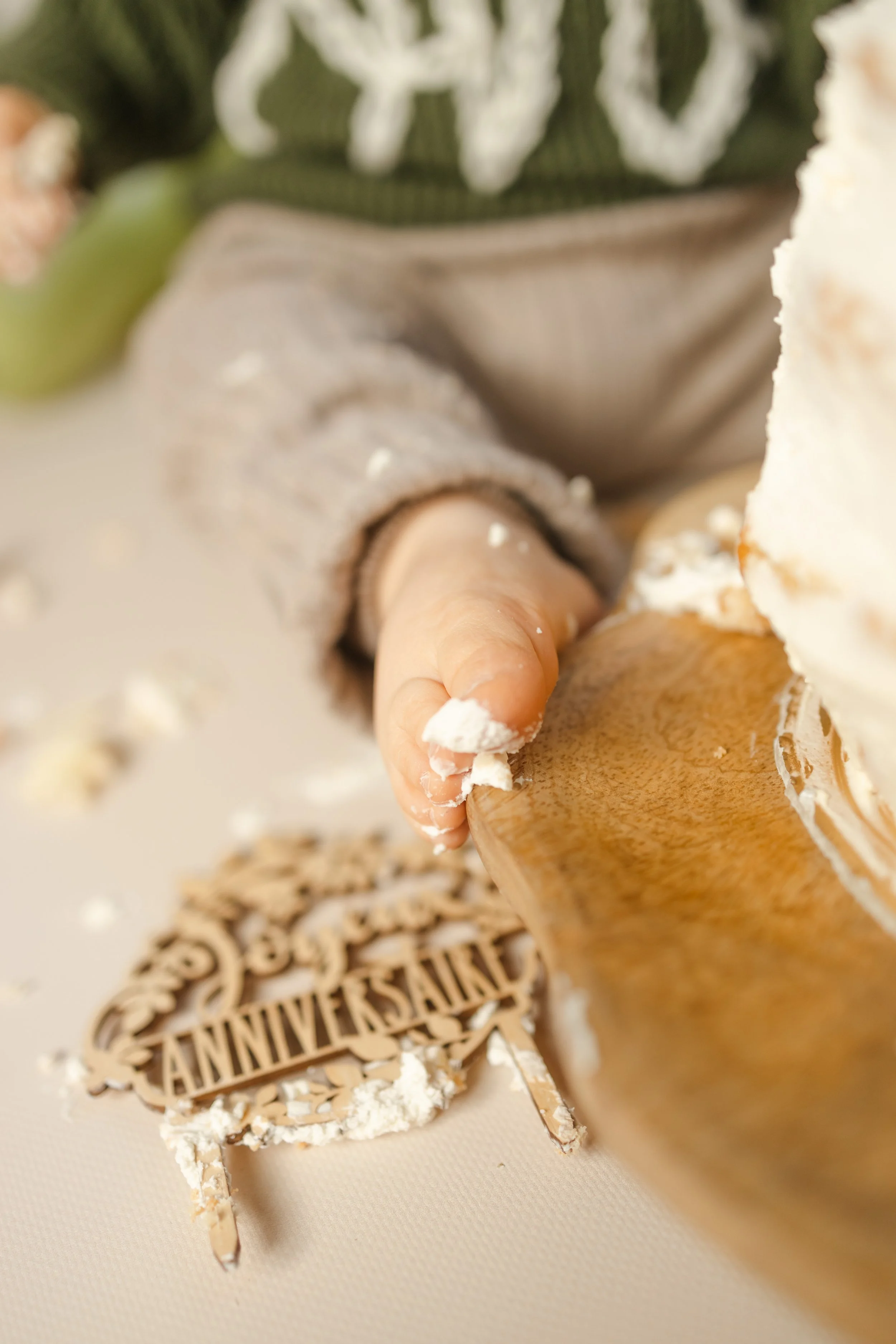 Main d'enfant touchant un gâteau avec un décor de fête d'anniversaire en bois et en fond une décoration avec un motif vert et blanc.