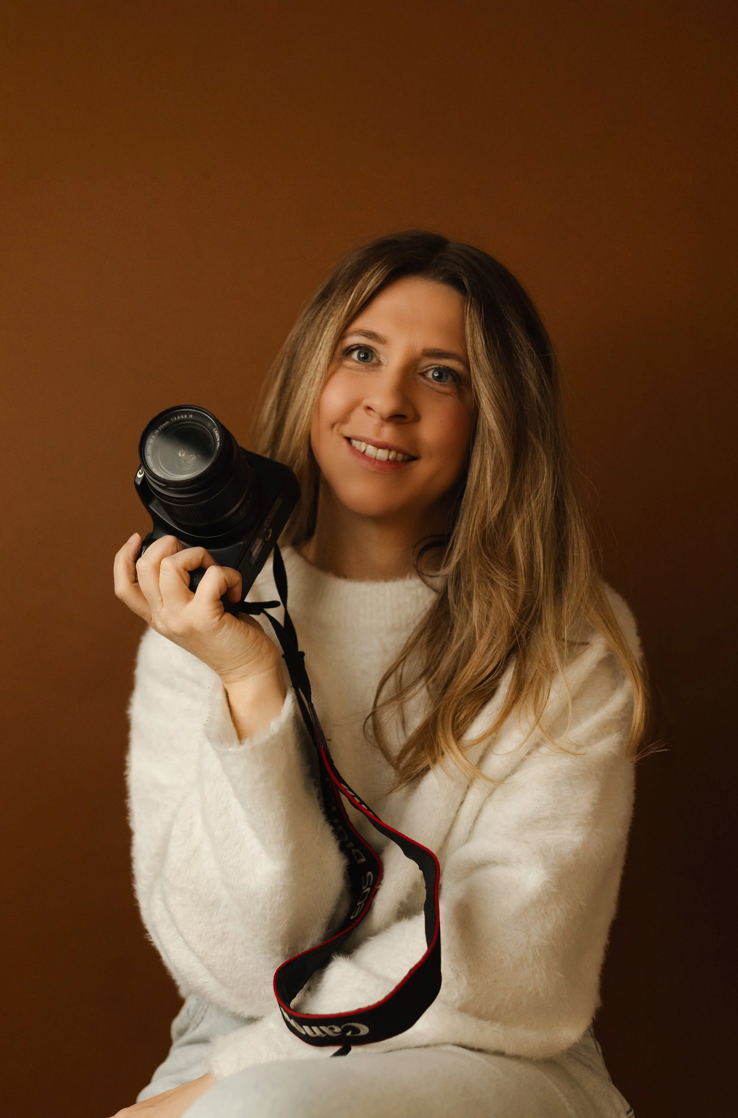 Femme souriante tenant un appareil photo noir avec un fond marron