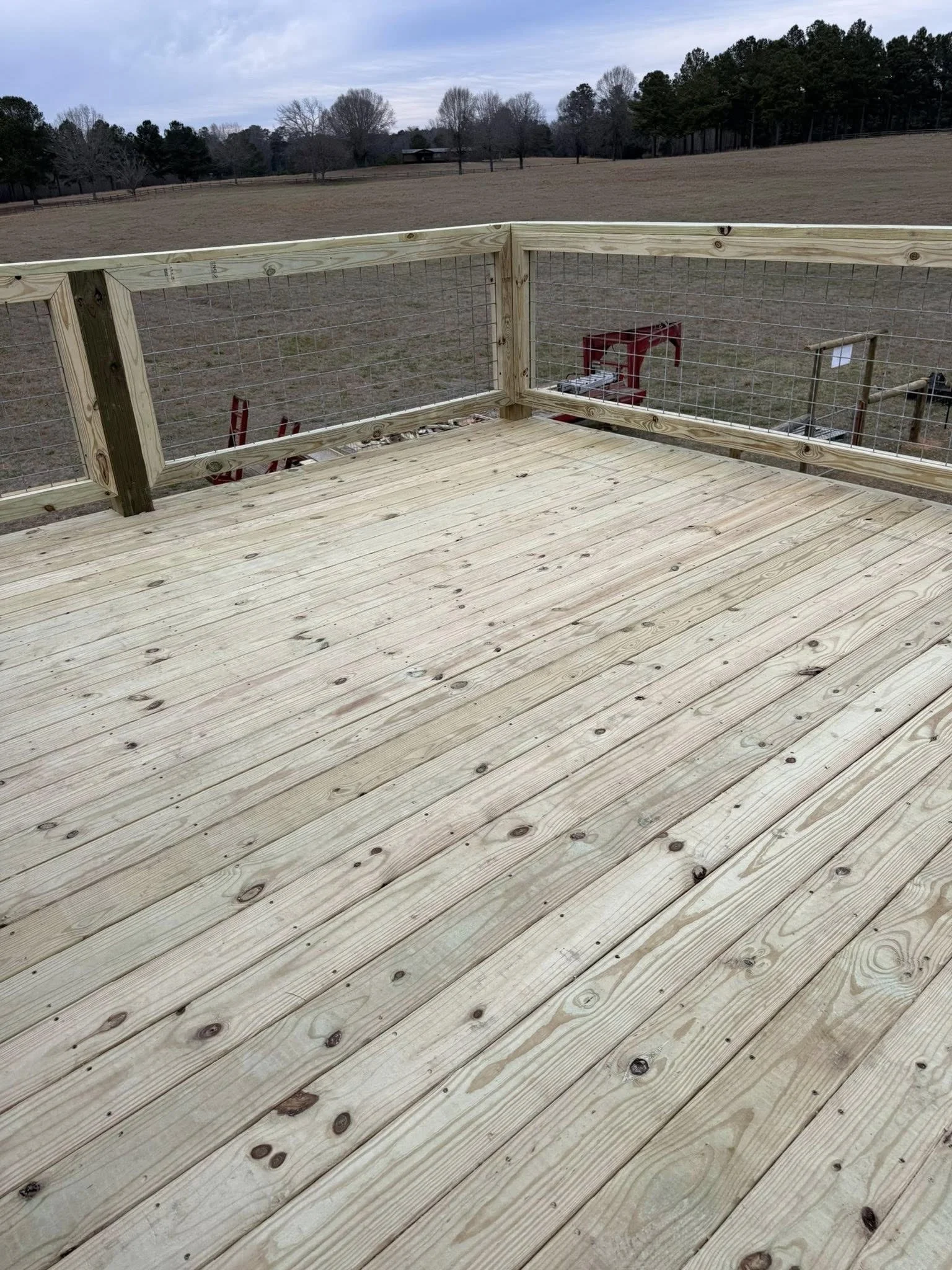 Empty wooden deck with a safety railing overlooking a field and trees in the distance.
