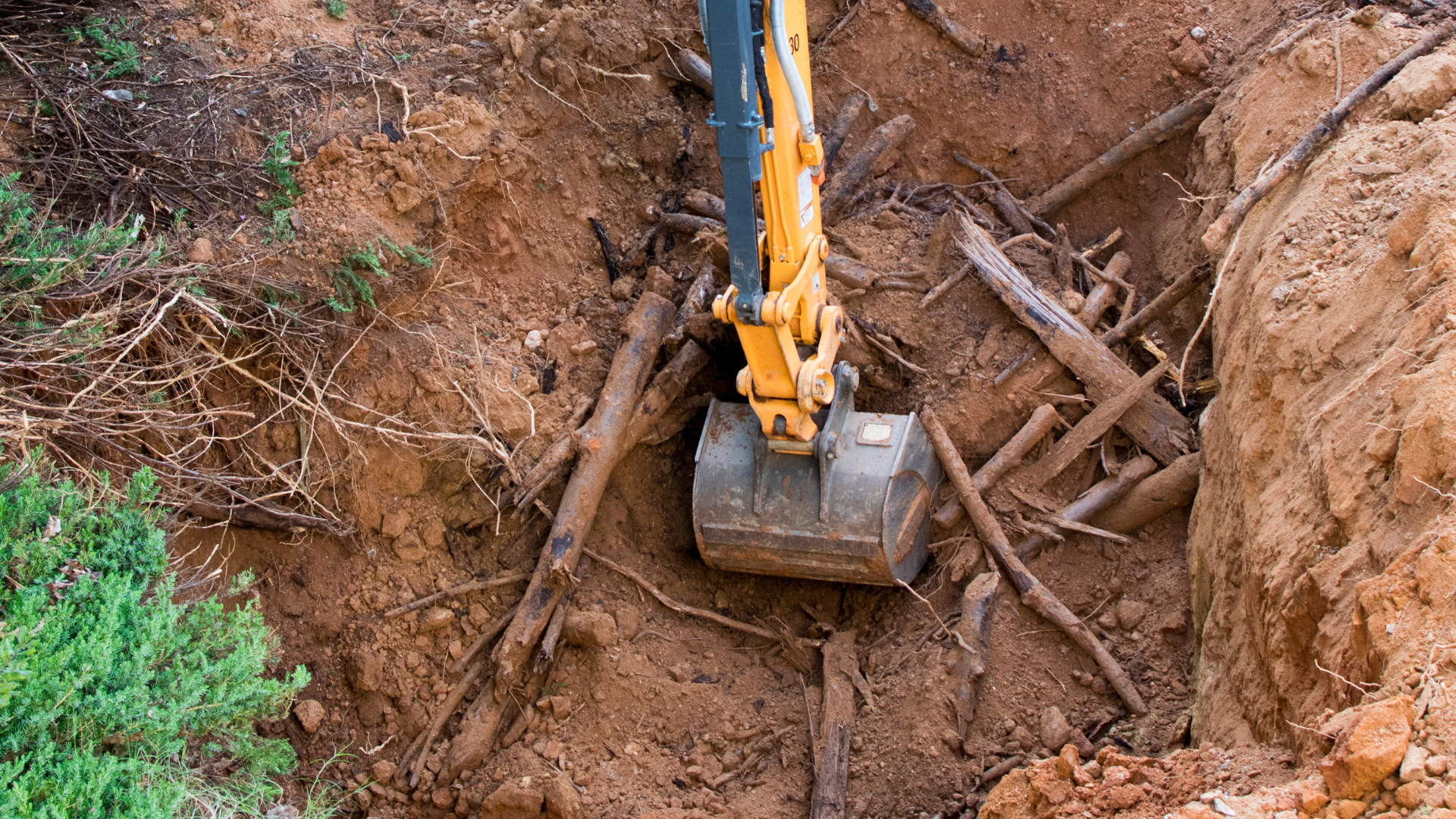 Excavator digging in a trench with wooden supports and soil around it.