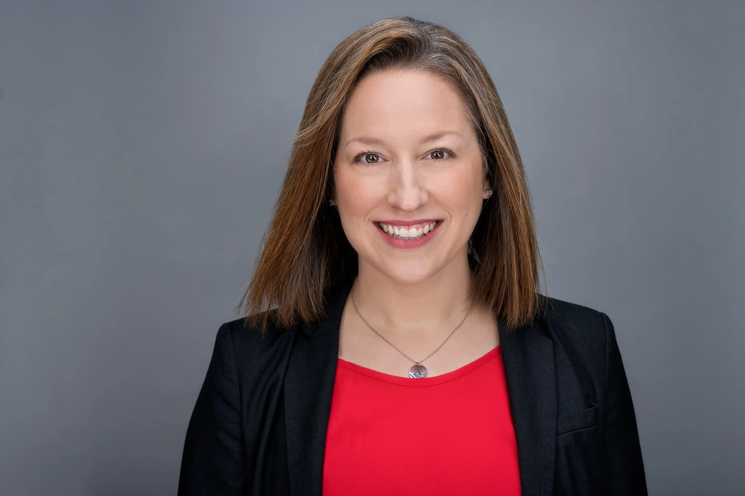 Headshot of Leanna McGrath wearing a red top and black blazer. Her hair is brown and shoulder lenght