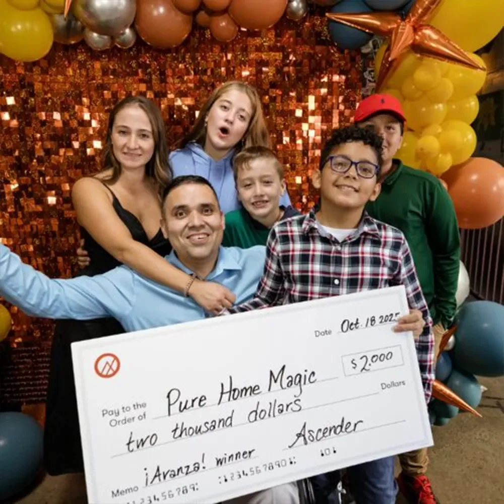 A group of six people celebrating with balloons and a shiny background, holding a giant check for two thousand dollars made out to Pure Home Magic, dated October 18, 2023, with the memo 'iAranza! winner' and the name Ascender. The scene appears joyful and festive.