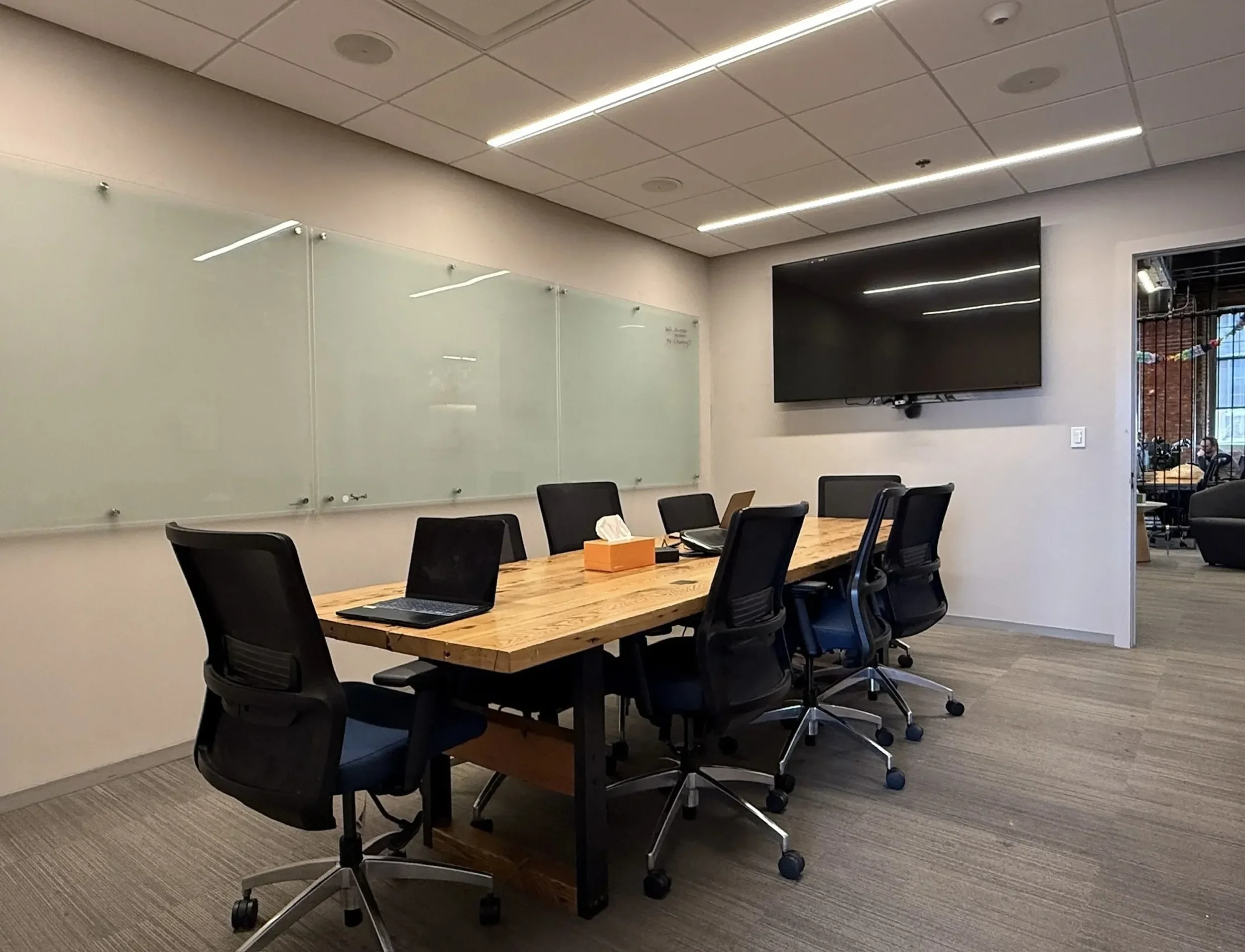 A photo of Ascender's primary conference room with a long wooden table surrounded by black office chairs. There is a whiteboard on the wall to the left and a large flat screen monitor mounted on the wall to the right.