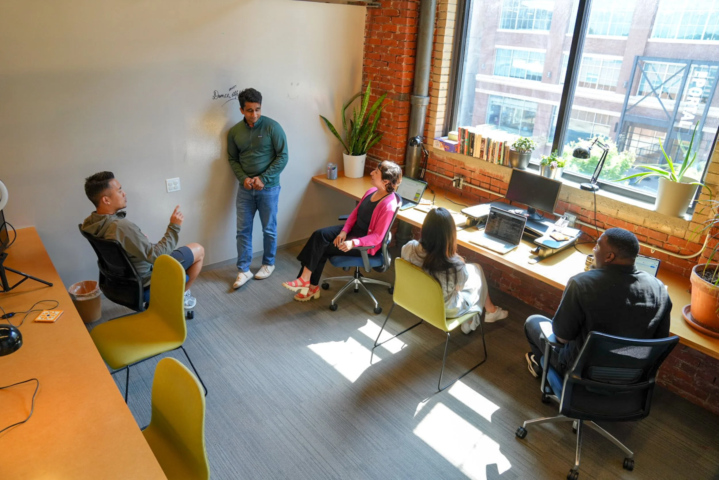 A photo of Ascender's lounge with several people sitting on gray sofas and chairs, some working on laptops. 