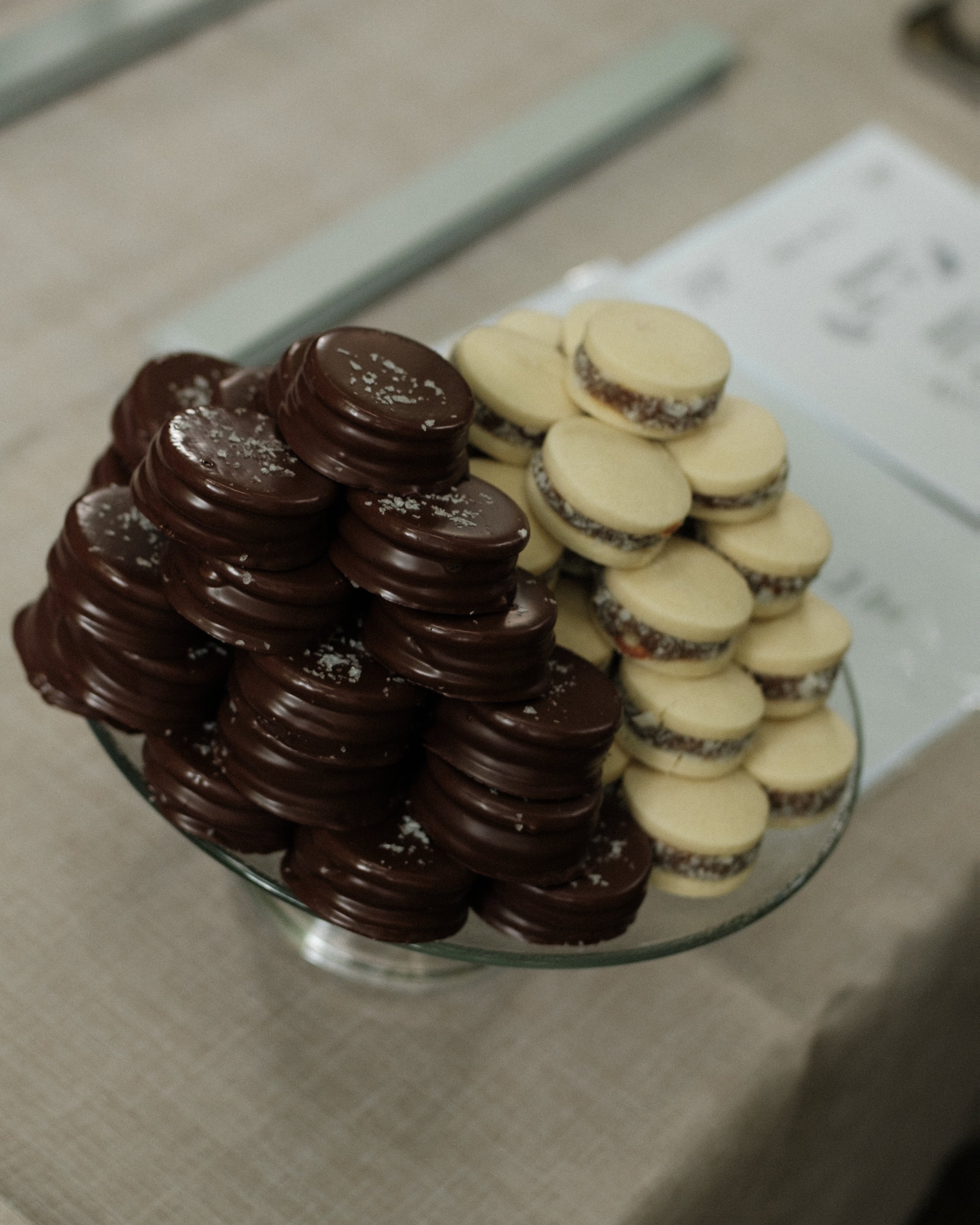 Two stacks of cookies, one with dark chocolate coating and the other with white chocolate coating, on a glass dish.