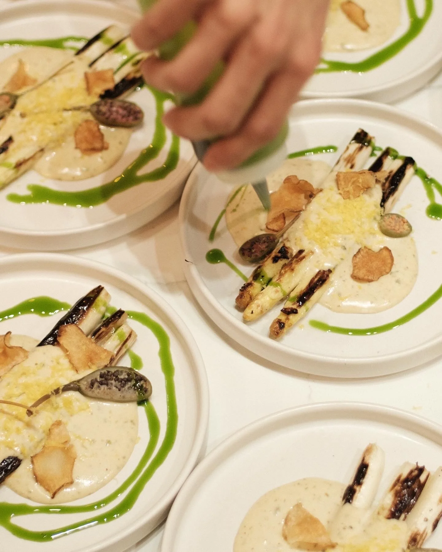 Plates of grilled asparagus with a creamy sauce, garnished with a green sauce, cheese, and crispy toppings.