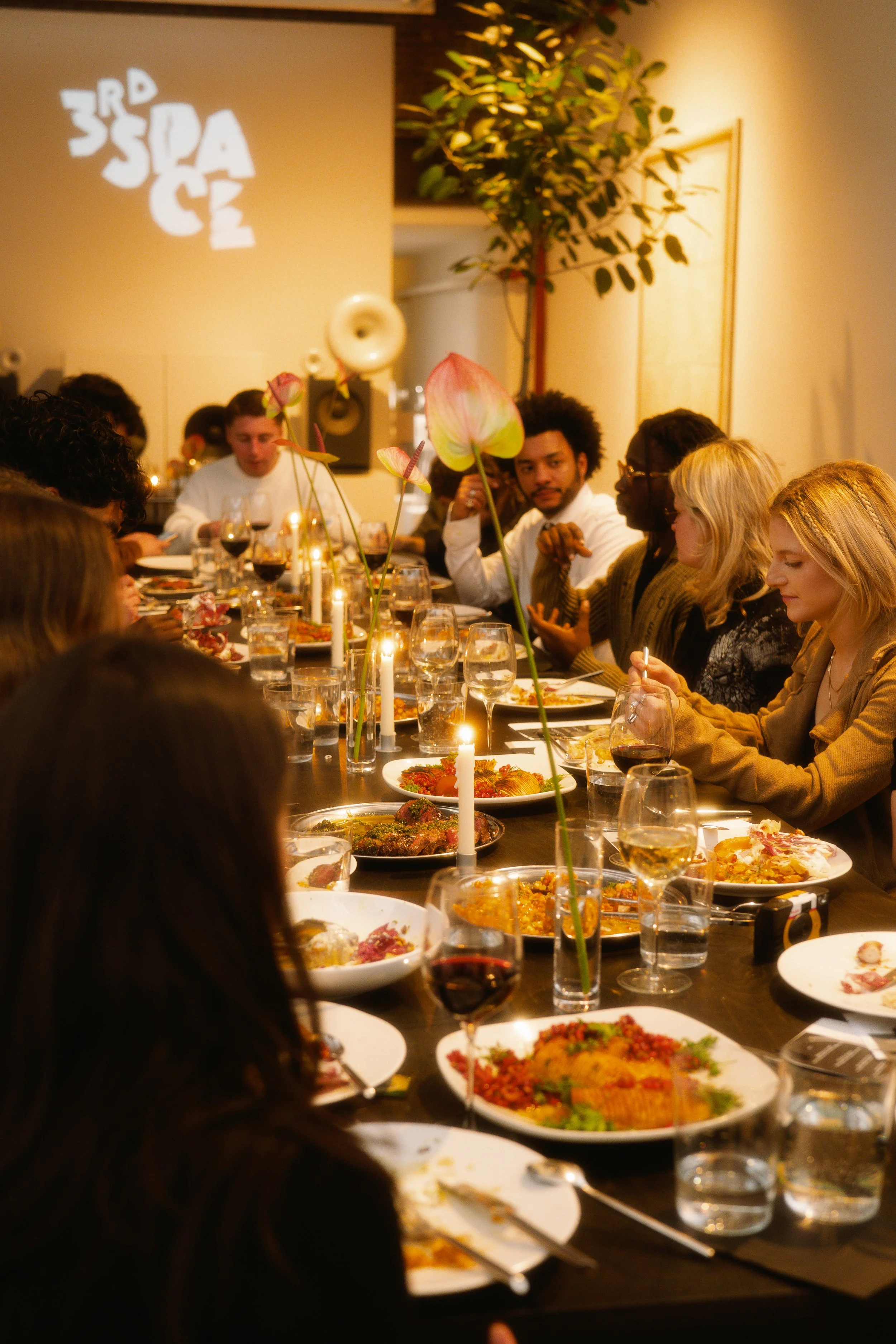 People gathered around a dining table having a meal, decorated with flowers and candles.