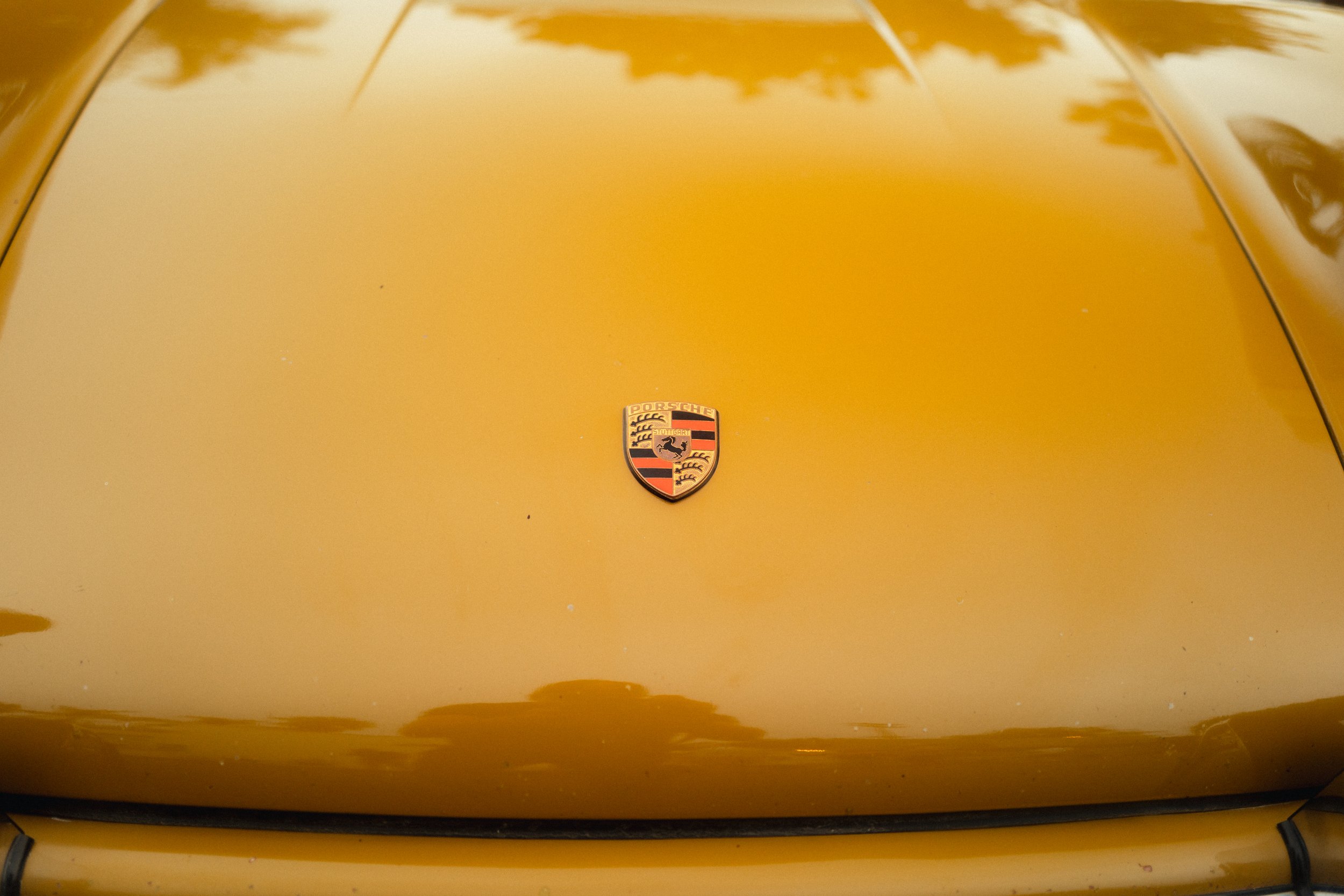 Close-up of a yellow Porsche car hood with a Porsche emblem in the center.
