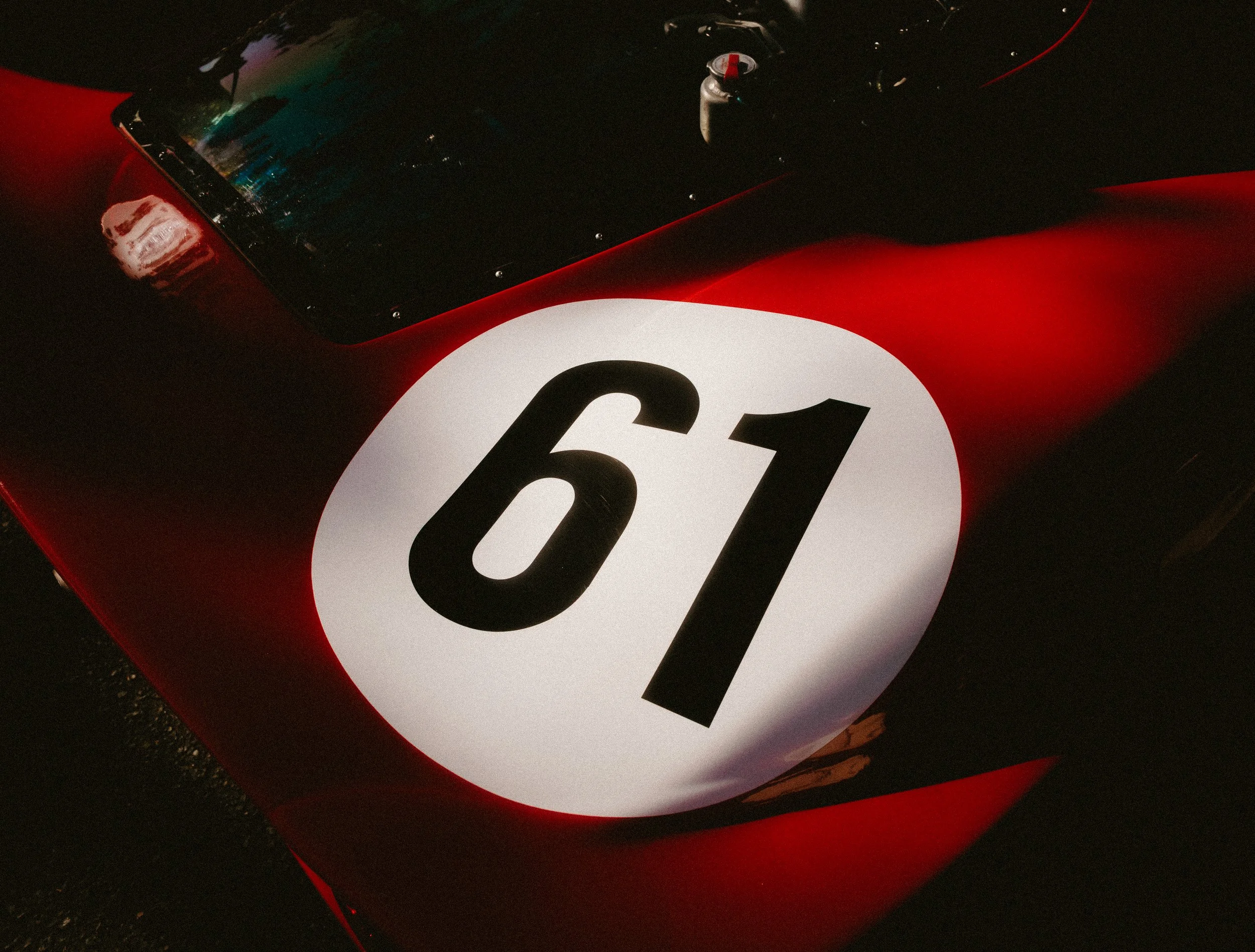 Close-up of a race car with a large white circle on the hood displaying the number 61 in black.
