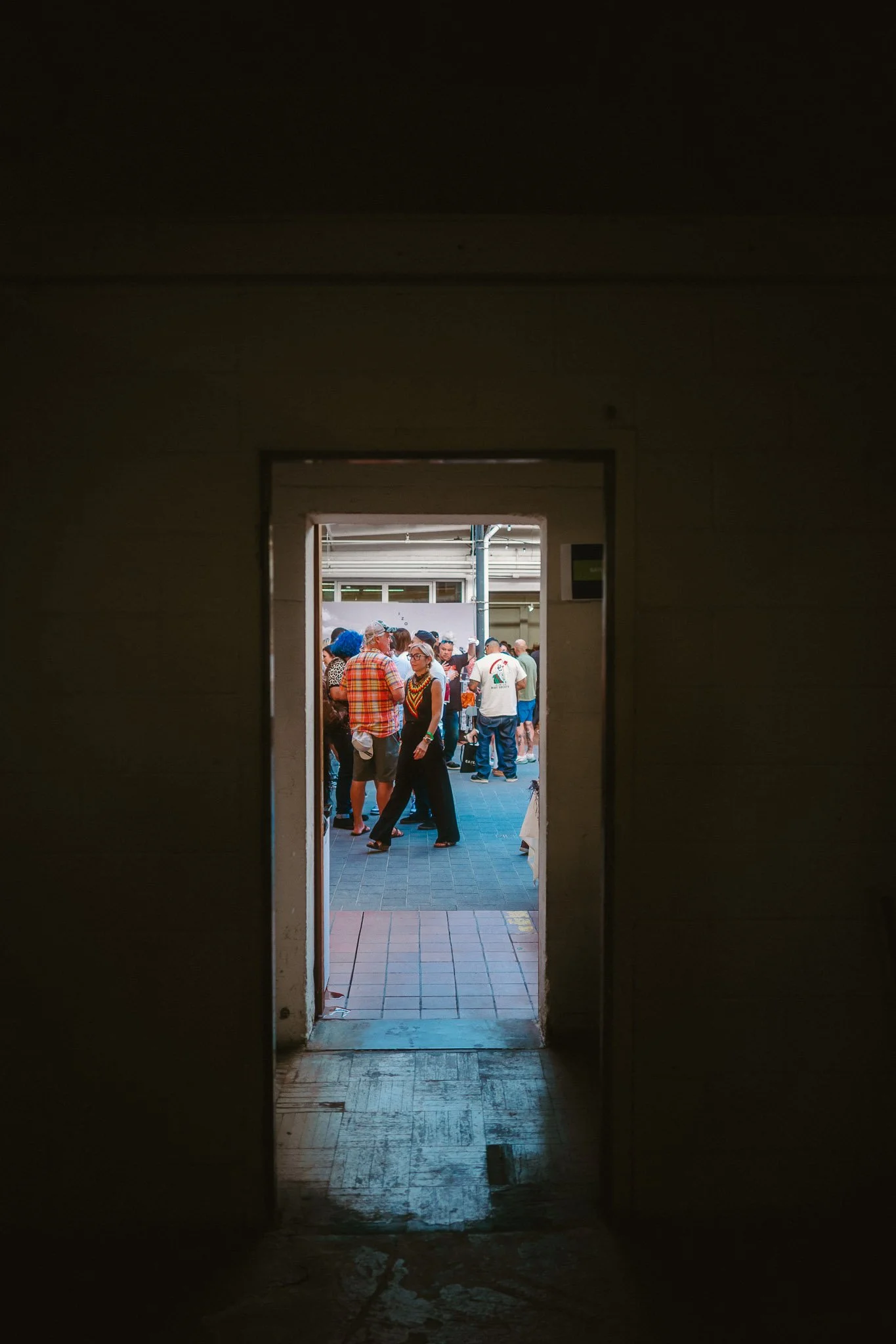 People gathered outdoors seen through a doorway, with some chatting and walking.