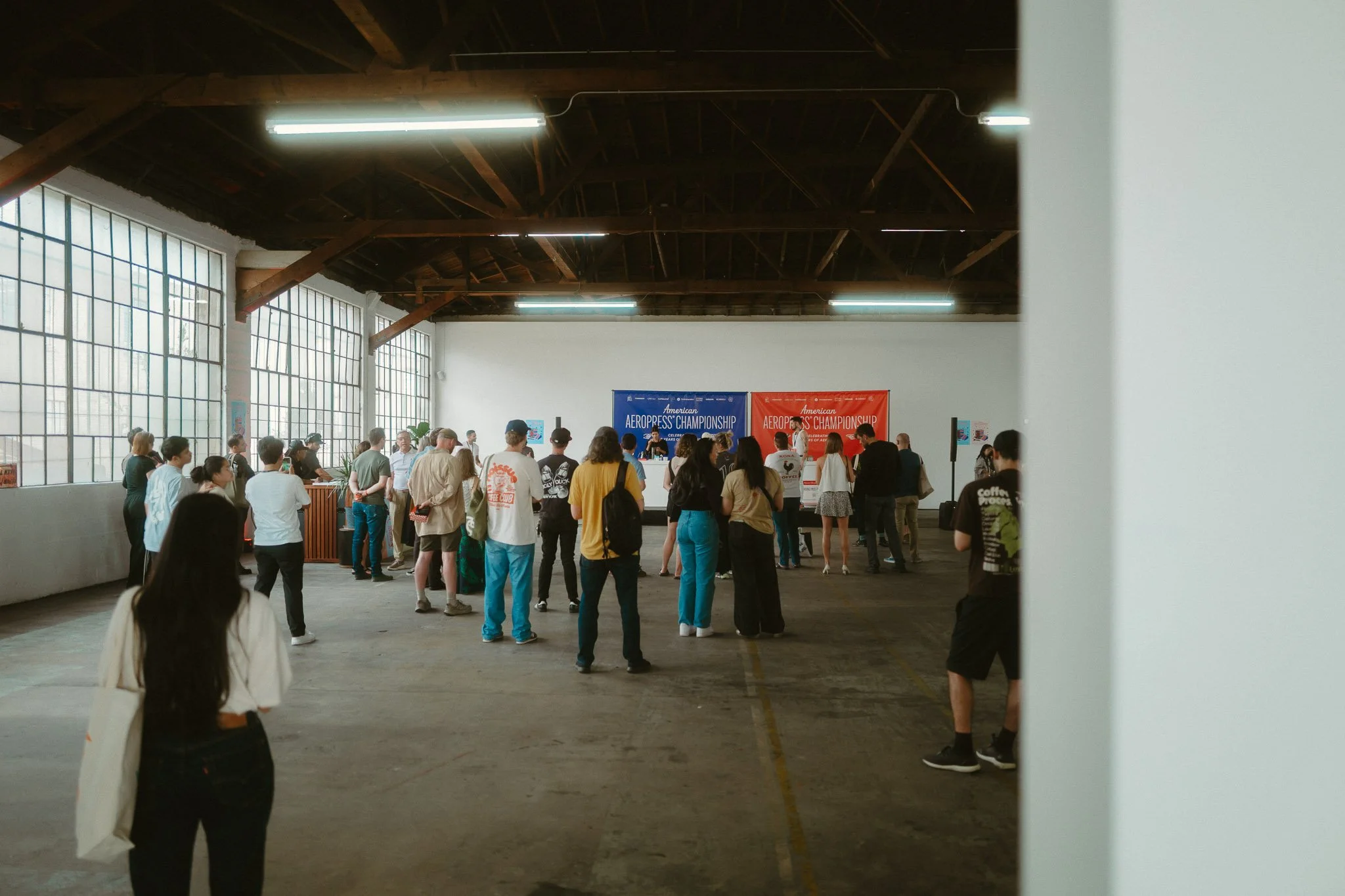 People gathered in a large indoor space with high ceilings, attending an event with event banners reading "American AeroPress Championship" in blue and red.