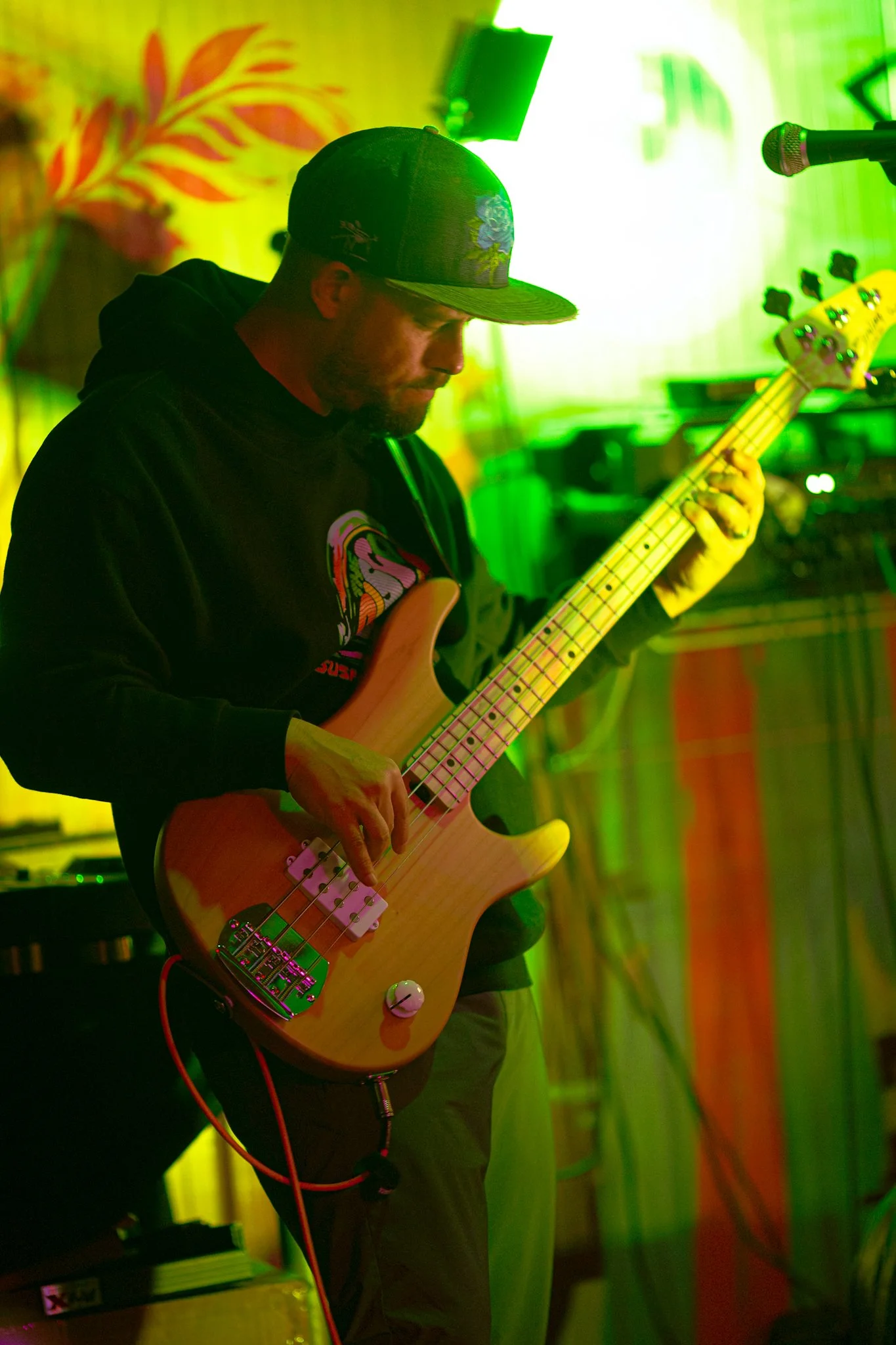 A man playing a bass guitar on stage with colorful green and yellow background lighting.