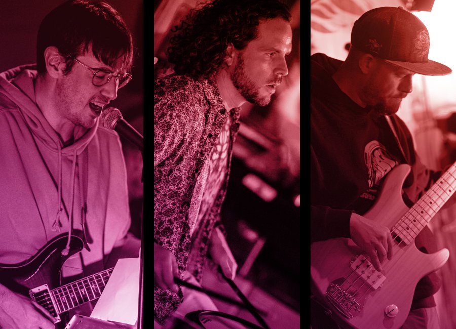Three male musicians performing with instruments, pink and red lighting.