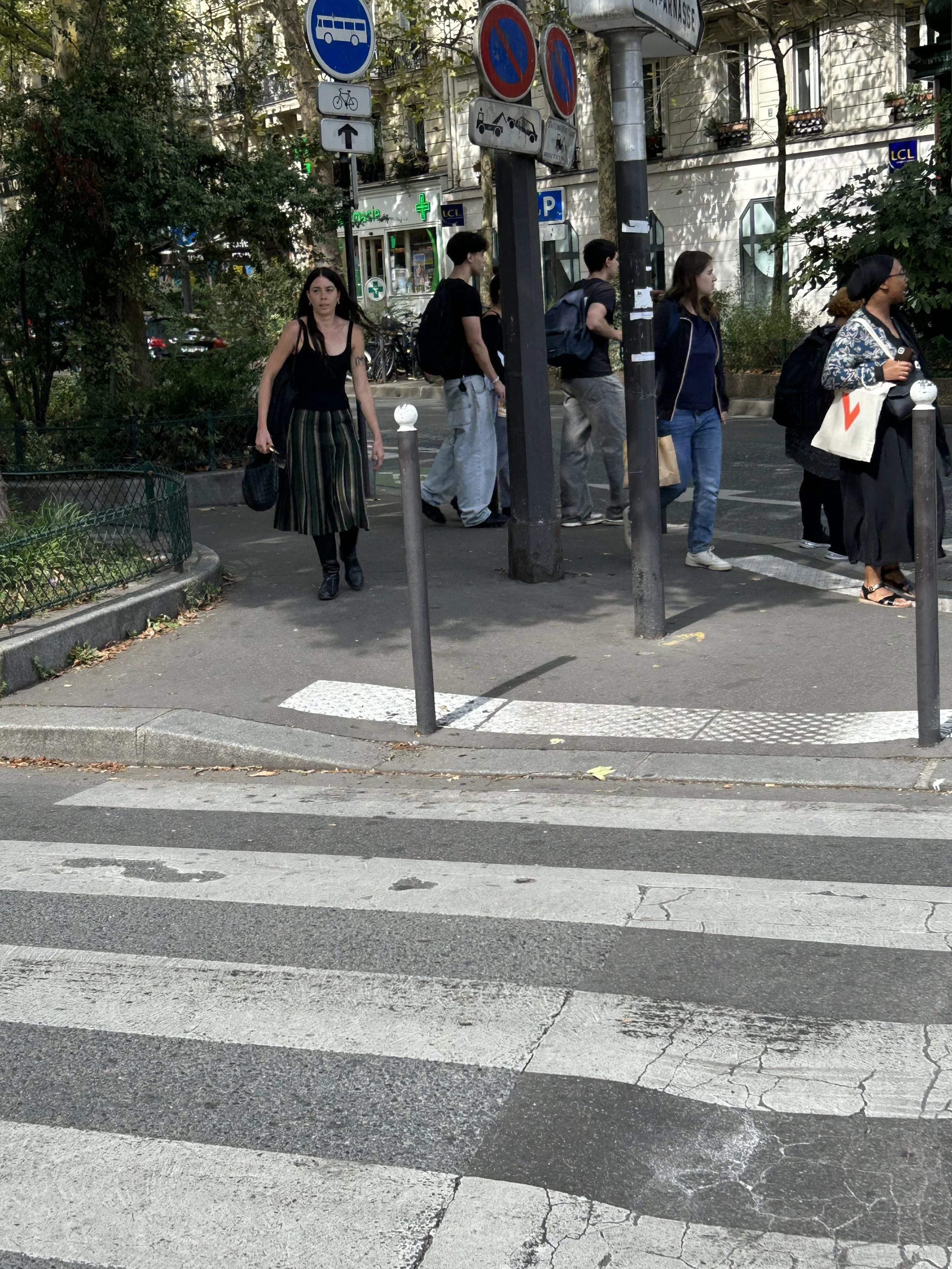 Pedestrians walking across a crosswalk at an intersection with street signs and a building in the background.