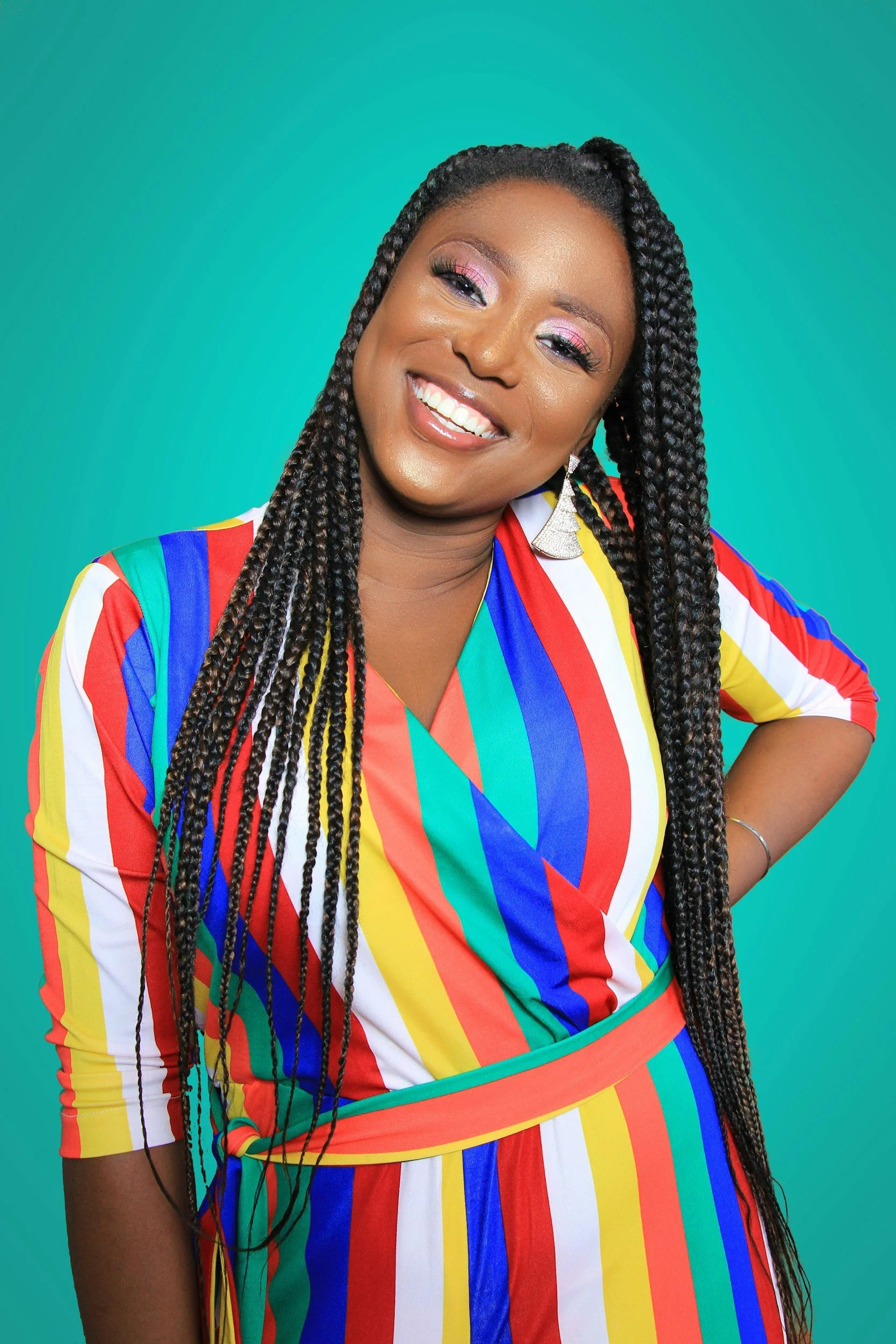 A woman with long braided hair, wearing colorful, striped clothing, smiling against a teal background.