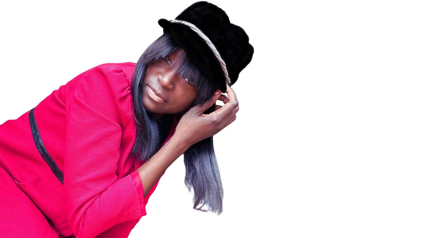 A woman with long dark purple hair wearing a black velvet hat with a silver band, a red jacket, and listening to music with one hand on her headphone.