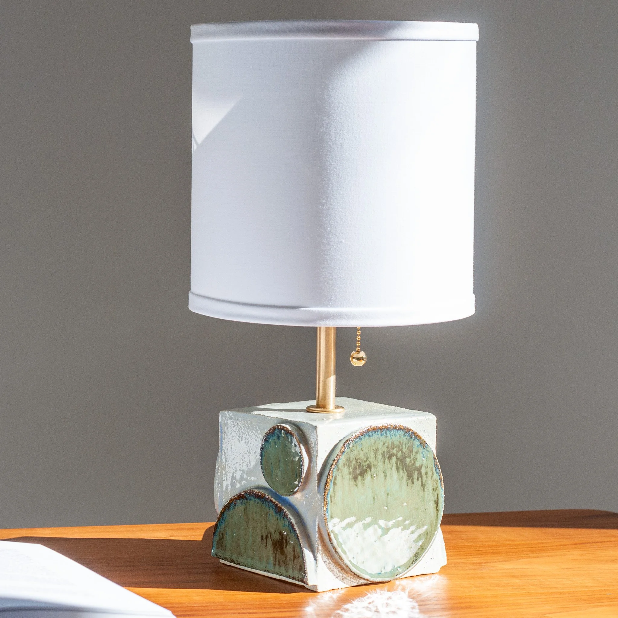 Geometria Table Lamp by Jim Schatz — intersecting ceramic volumes on a cubic base, with a white linen shade.