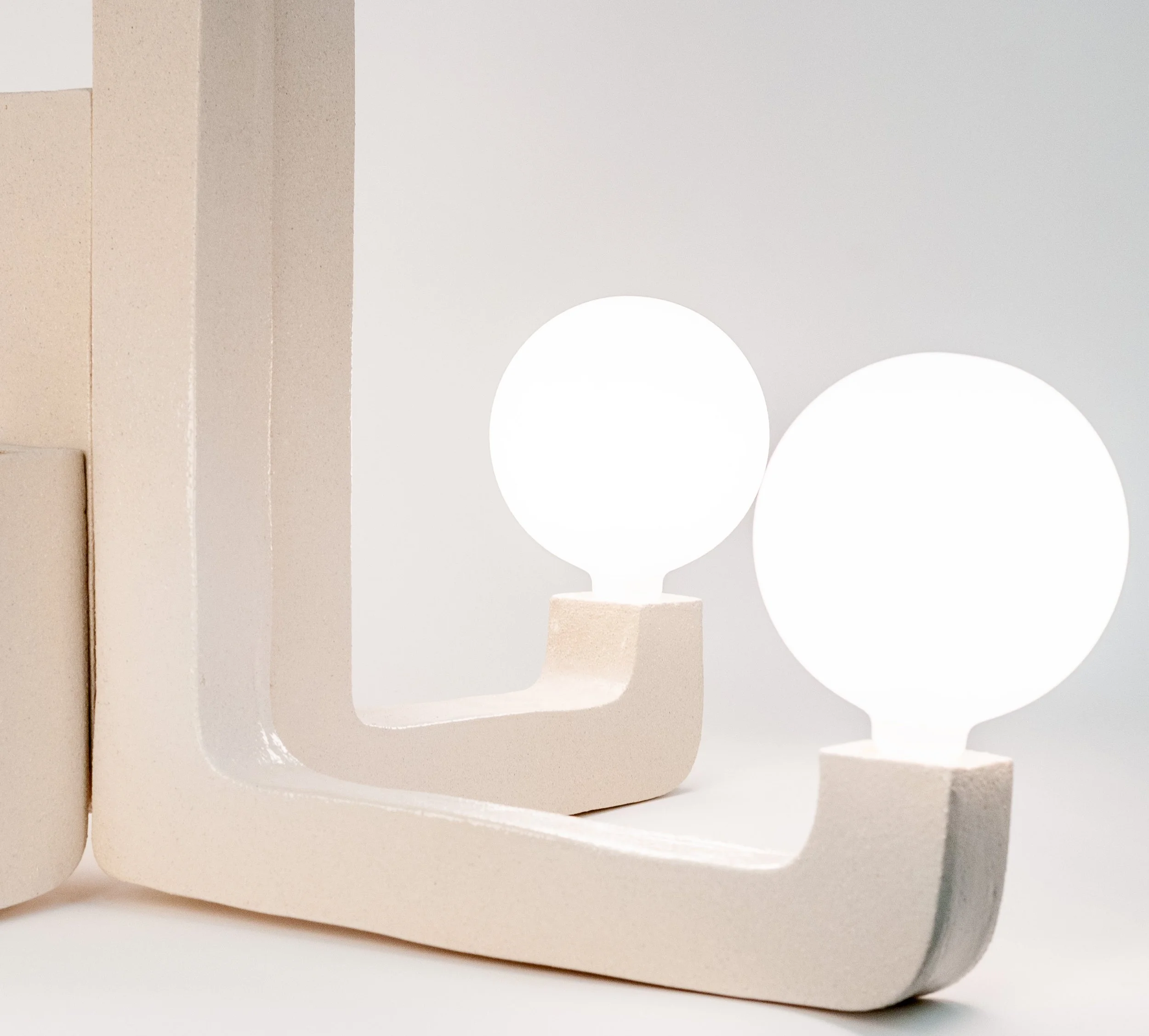 our Arm Chandelier by Jim Schatz — close detail of two lit globes and textured stoneware arms