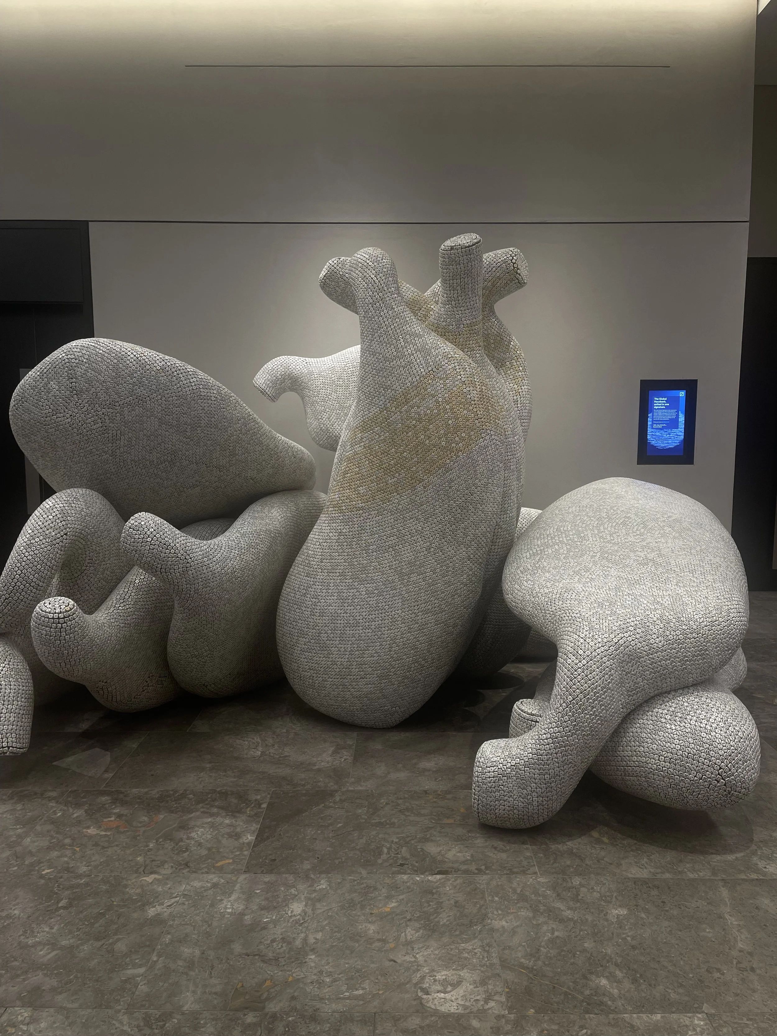 Abstract sculpture resembling a human heart with intricate surface textures and curving, organic shapes, placed indoors on a gray-tiled floor.