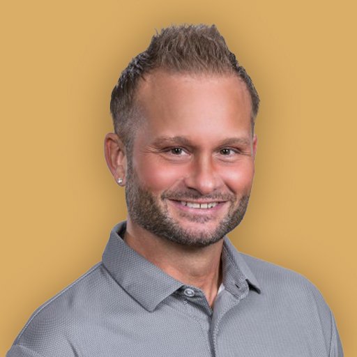 A professional headshot of a smiling man in a black suit and white shirt against a beige background.