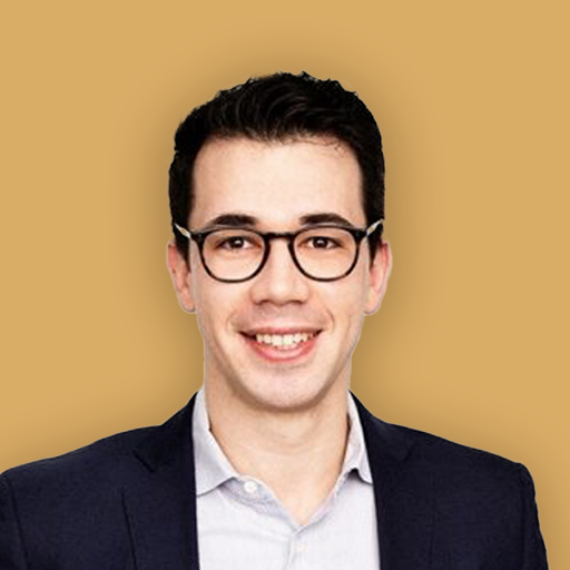 A smiling man wearing glasses, a dark blazer, and a light-colored shirt against a plain background.