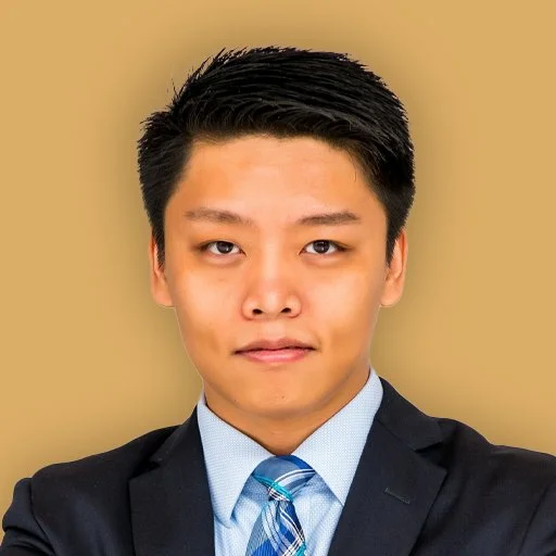 Professional portrait of a young Asian man in a suit and tie with a neutral expression against a plain background.