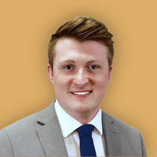 A portrait of a smiling man in a suit against a beige background.