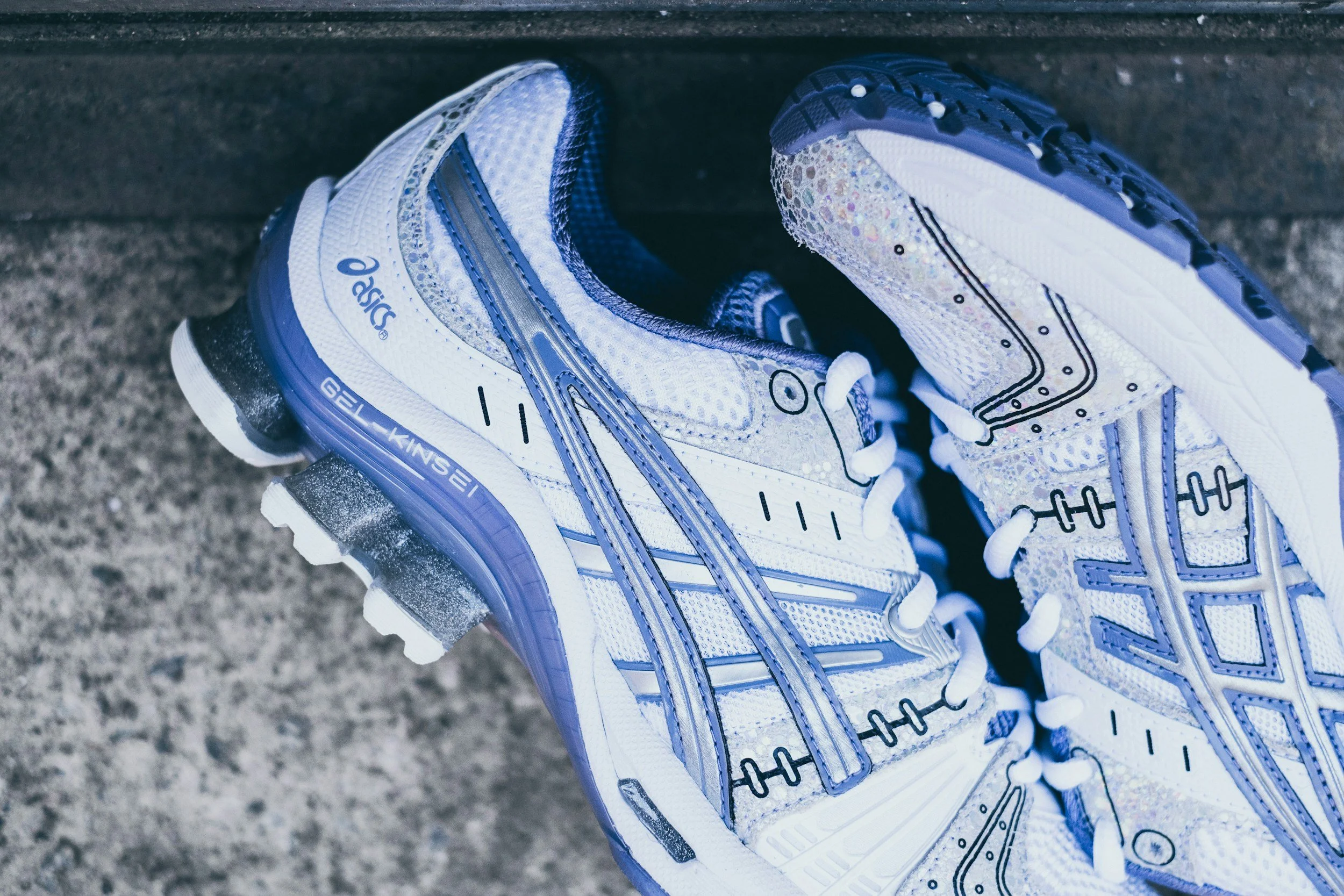 Pair of white and blue ASICS GEL-Kinsei running shoes on a textured ground.