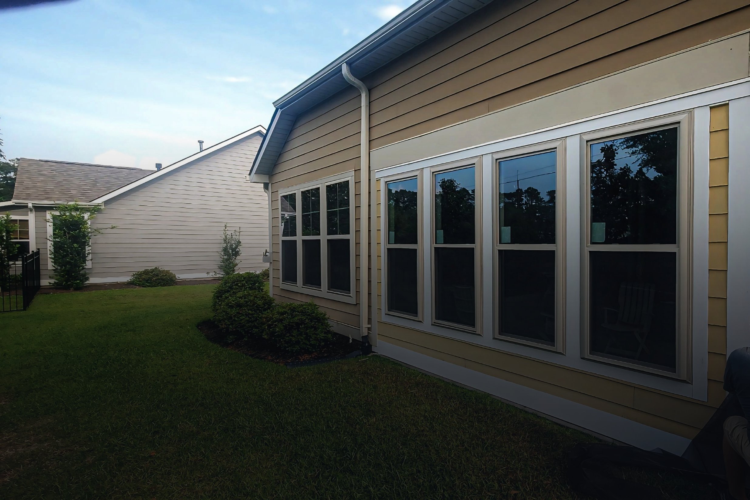 Side view of a house with beige siding, multiple windows, and some bushes in the yard.