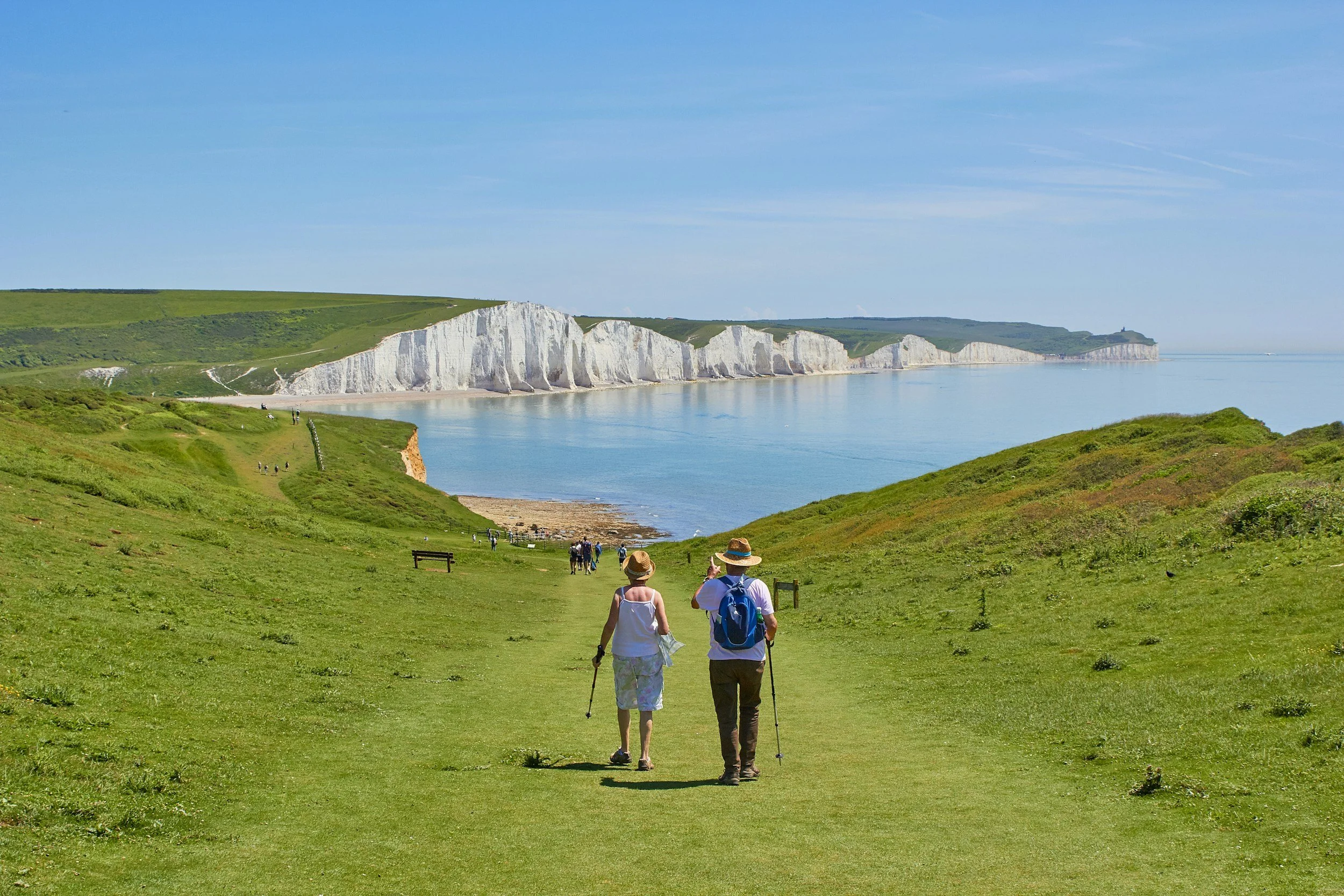 People walking along a grassy path with white cliffs and the ocean in the background.