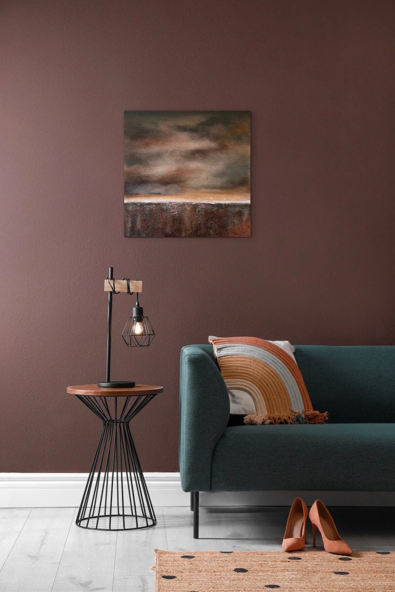 Modernes Wohnzimmer mit turbulenter, dunkler Wand, Kunstwerk an der Wand, blaues Sofa mit buntem Kissen, kleiner Beistelltisch mit Stehlampe, braune High Heels auf Teppich.