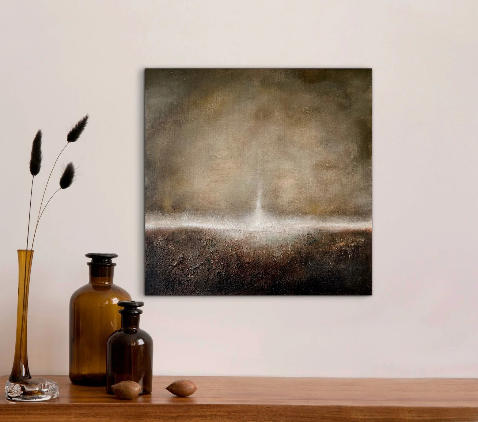 Abstraktes Gemälde an einer weißen Wand, daneben auf einem Holztisch eine braune Glasvase mit drei schwarzen Trockenpflanzen, zwei kleinere braune Flaschen und zwei Steine.