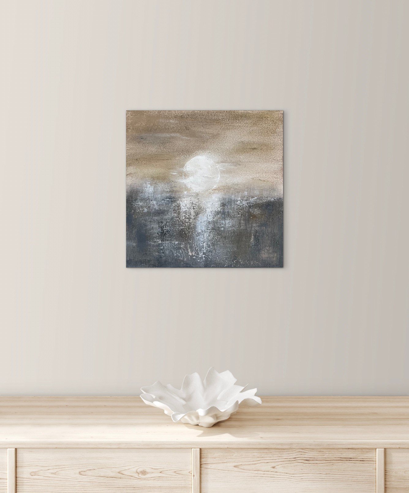 Ein abstraktes Gemälde an einer weißen Wand, darunter eine weiße, Blüten-ähnliche Dekoration auf einem Holztisch.