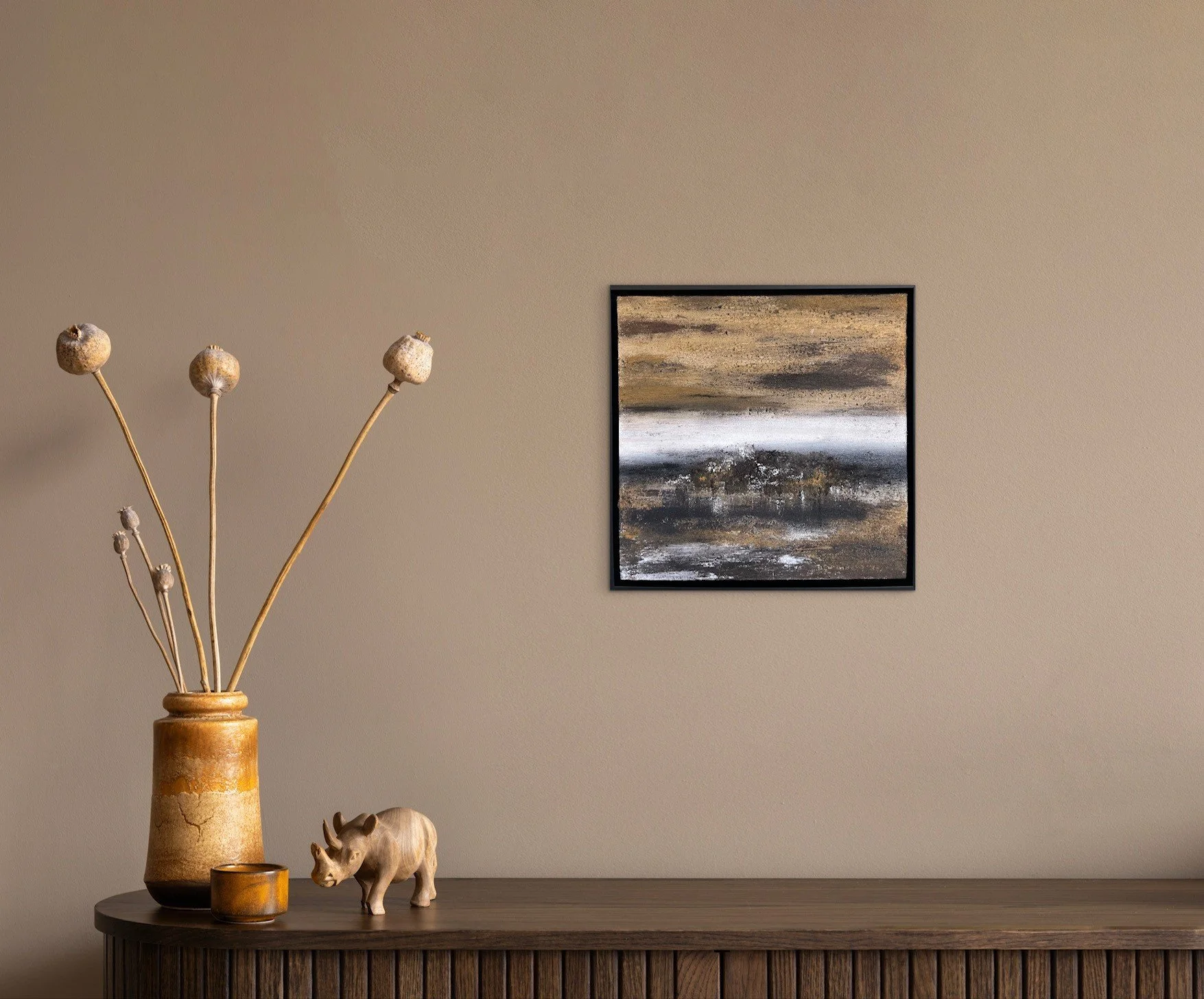 Inneneinrichtung mit brauner Vasen, getrockneten Strohhalmen, einem kleinen Elefantenmodell, Kerzen und einem Wandbild in neutralen Farben.