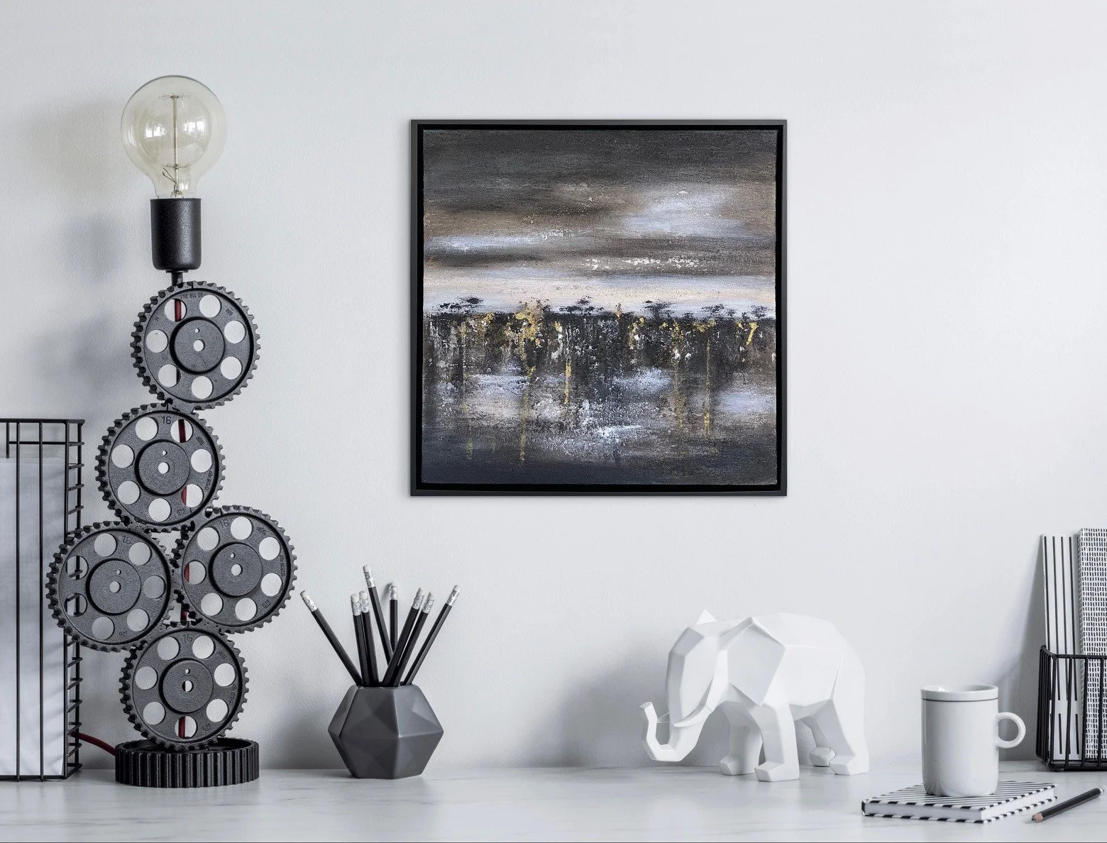 Schreibtisch mit dekorativen Gegenständen, darunter eine Skulptur eines Elefanten, eine Tasse, ein Notizblock und Stifte, vor einer weißen Wand mit einem abstrakten Gemälde.