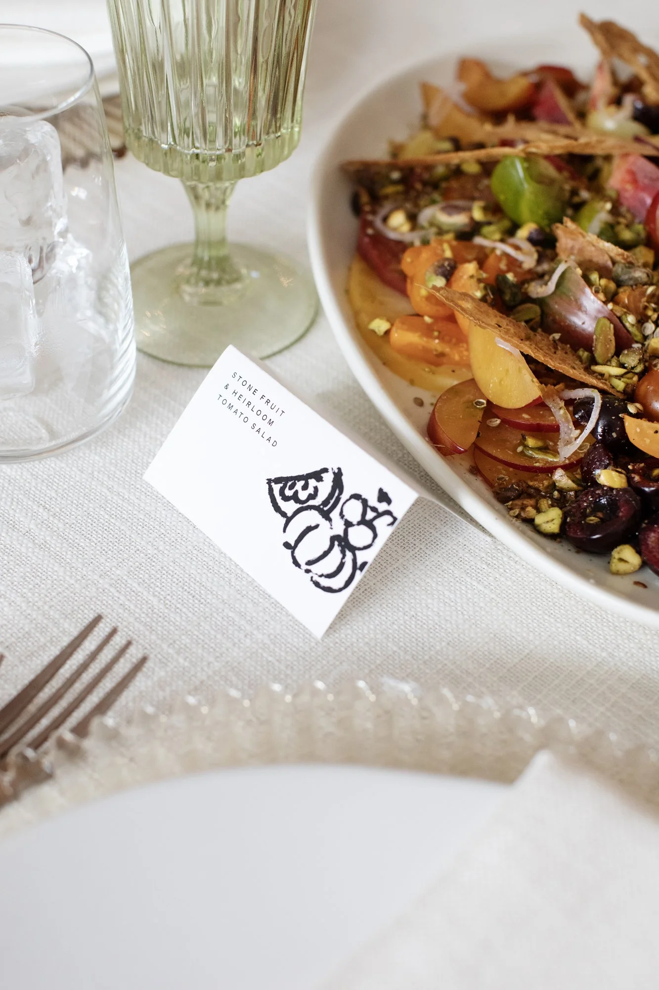 Family-style stone fruit and heirloom tomato salad with pistachios and a menu card on a wedding reception table — Food Gallery Catering Minneapolis