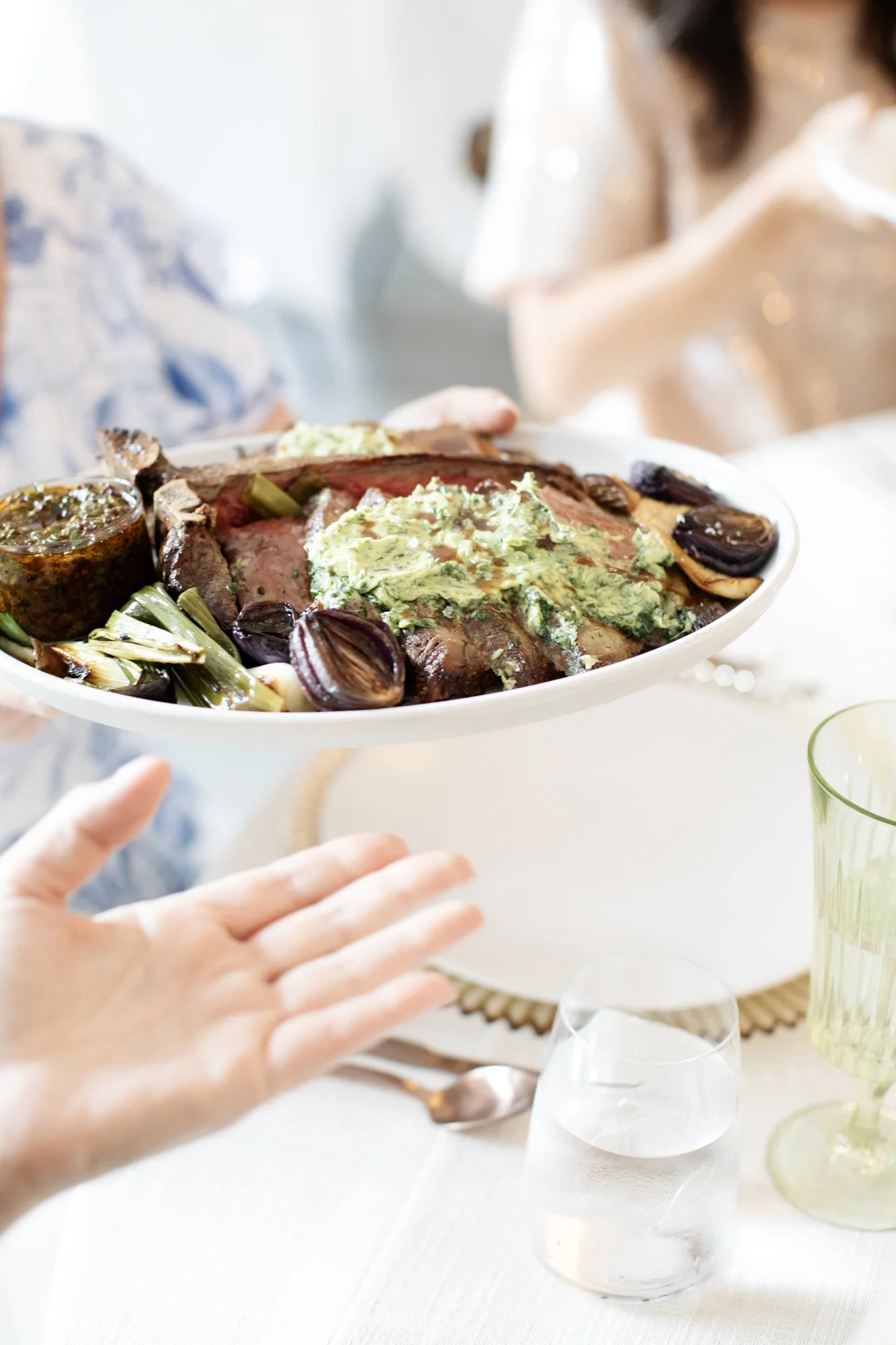 Guests passing a family-style platter of sliced steak with herb butter and roasted vegetables at a wedding reception — Food Gallery Catering Minneapolis