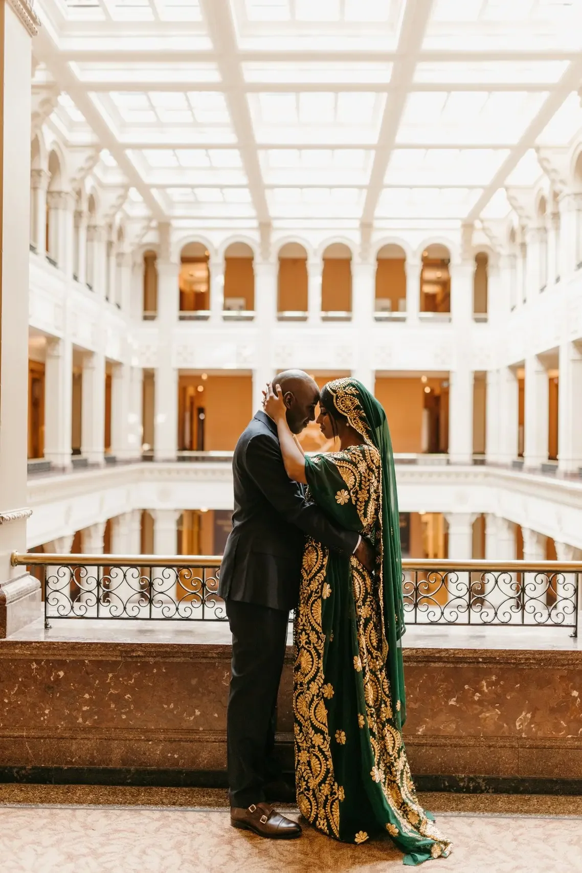 Wedding couple embraces in the natural light on a balcony at the Landmark Center, one of the best winter wedding venues in St. Paul, Minnesota