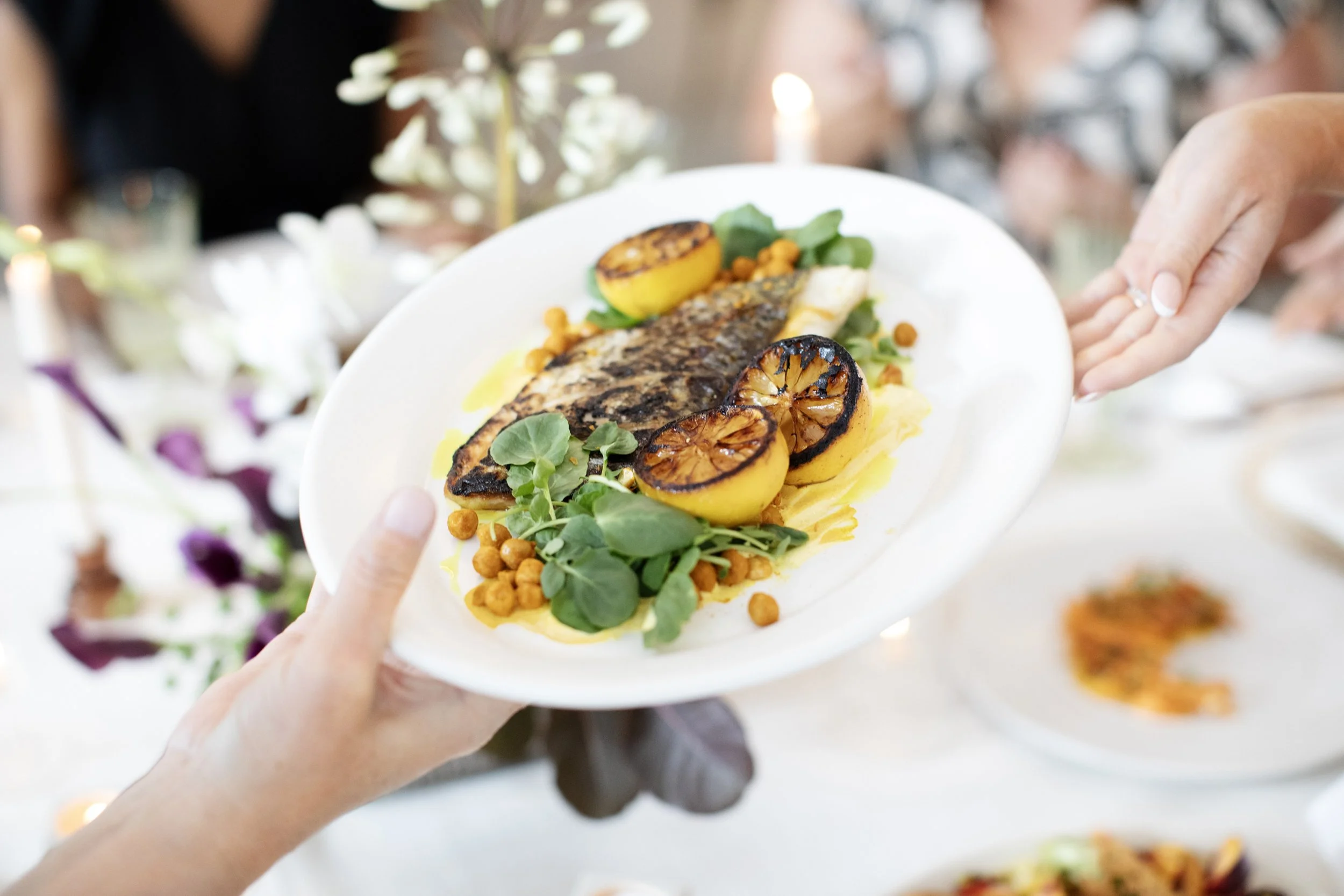 Guests passing a family-style fish dish at a wedding reception — Food Gallery Catering Minneapolis