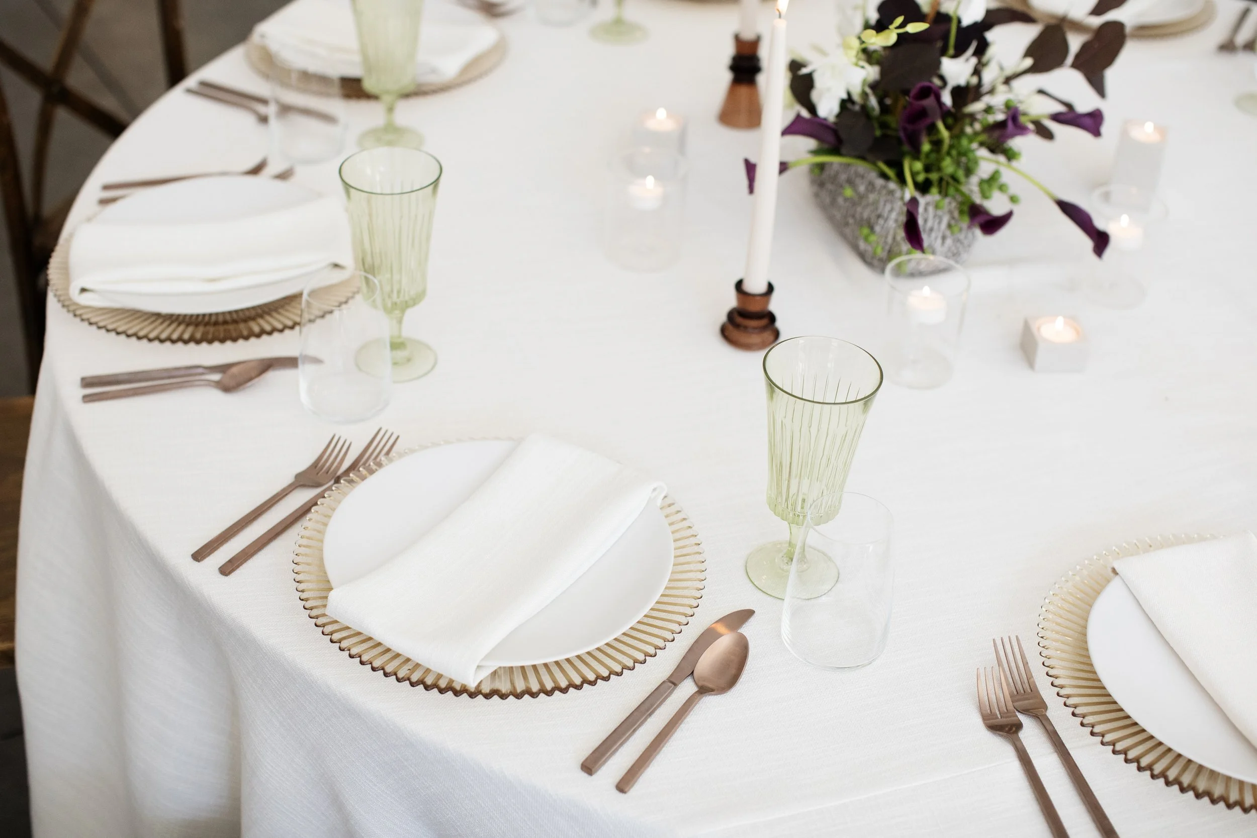 Elegant wedding reception table setting with gold charger plates, green glassware, copper flatware, and floral centerpiece — unique wedding venue Minnesota