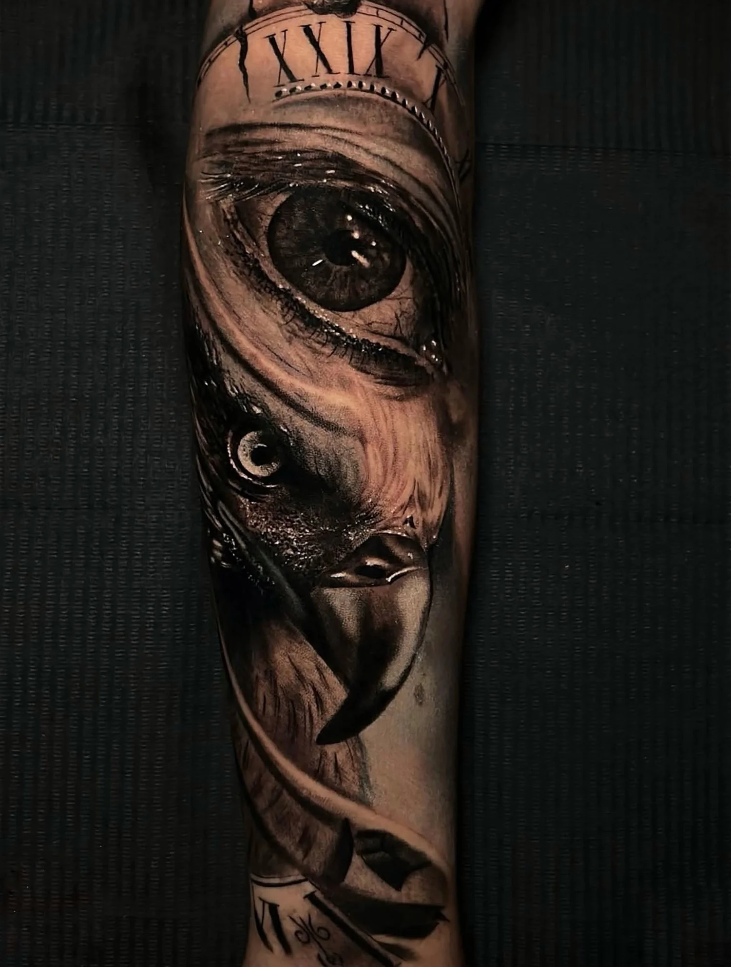 A realistic black and gray tattoo of a human eye on a forearm, with Roman numerals and other elements.